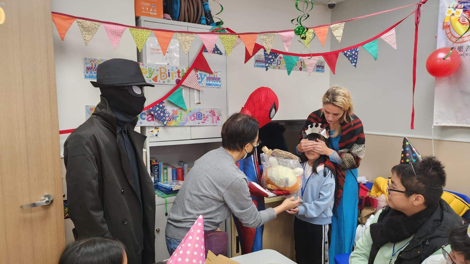 Adults help a child receive a gift beside costumed performers.