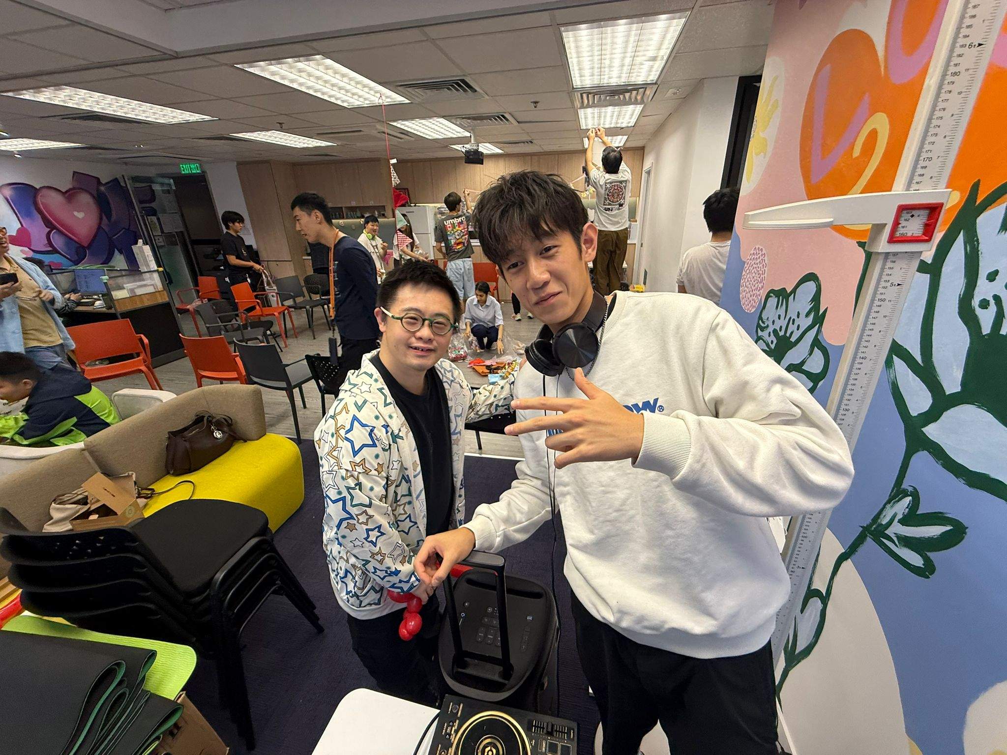 Two people pose together beside a stack of chairs.