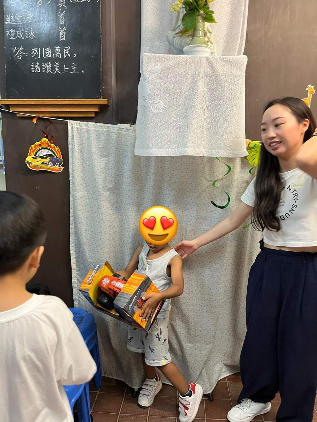 An adult stands beside a child holding a boxed toy.
