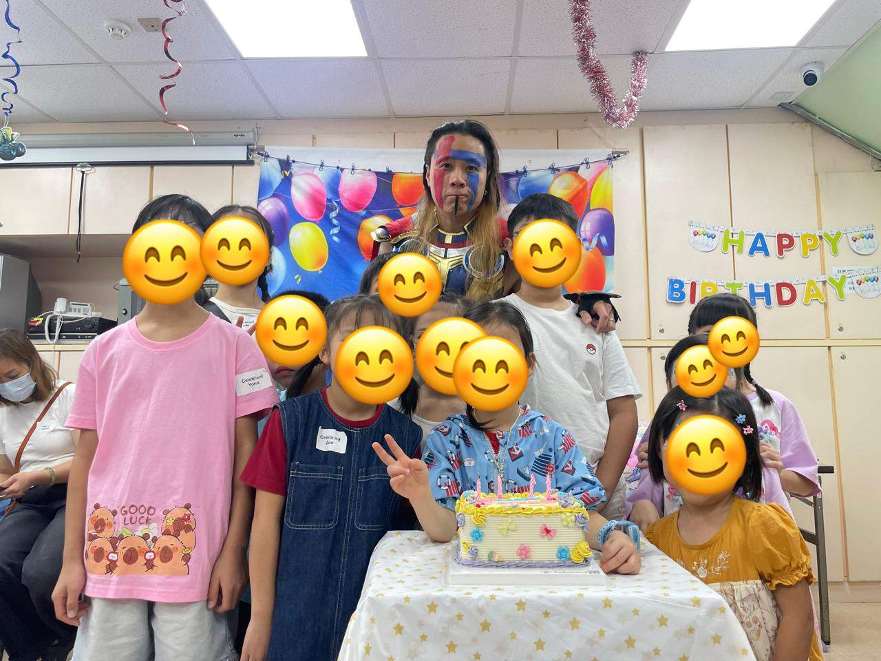 Children and a costumed performer gather behind a decorated cake.