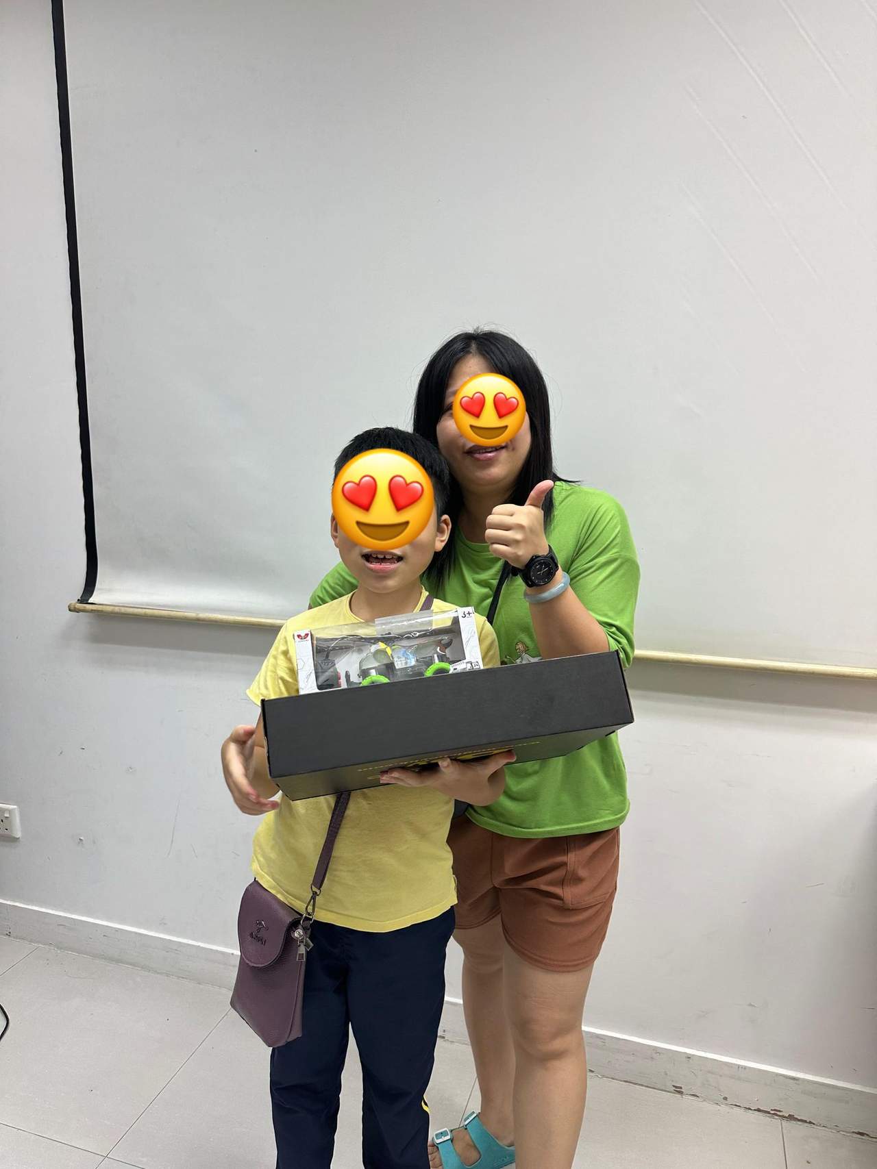 An adult stands behind a child holding a long boxed gift.