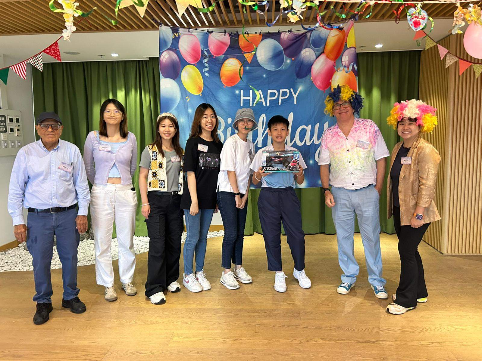 A group of adults poses beneath the decorated birthday backdrop.