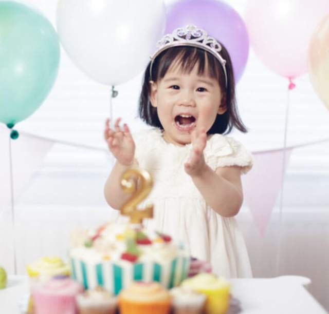 A child stands behind cupcakes beneath pastel balloons.