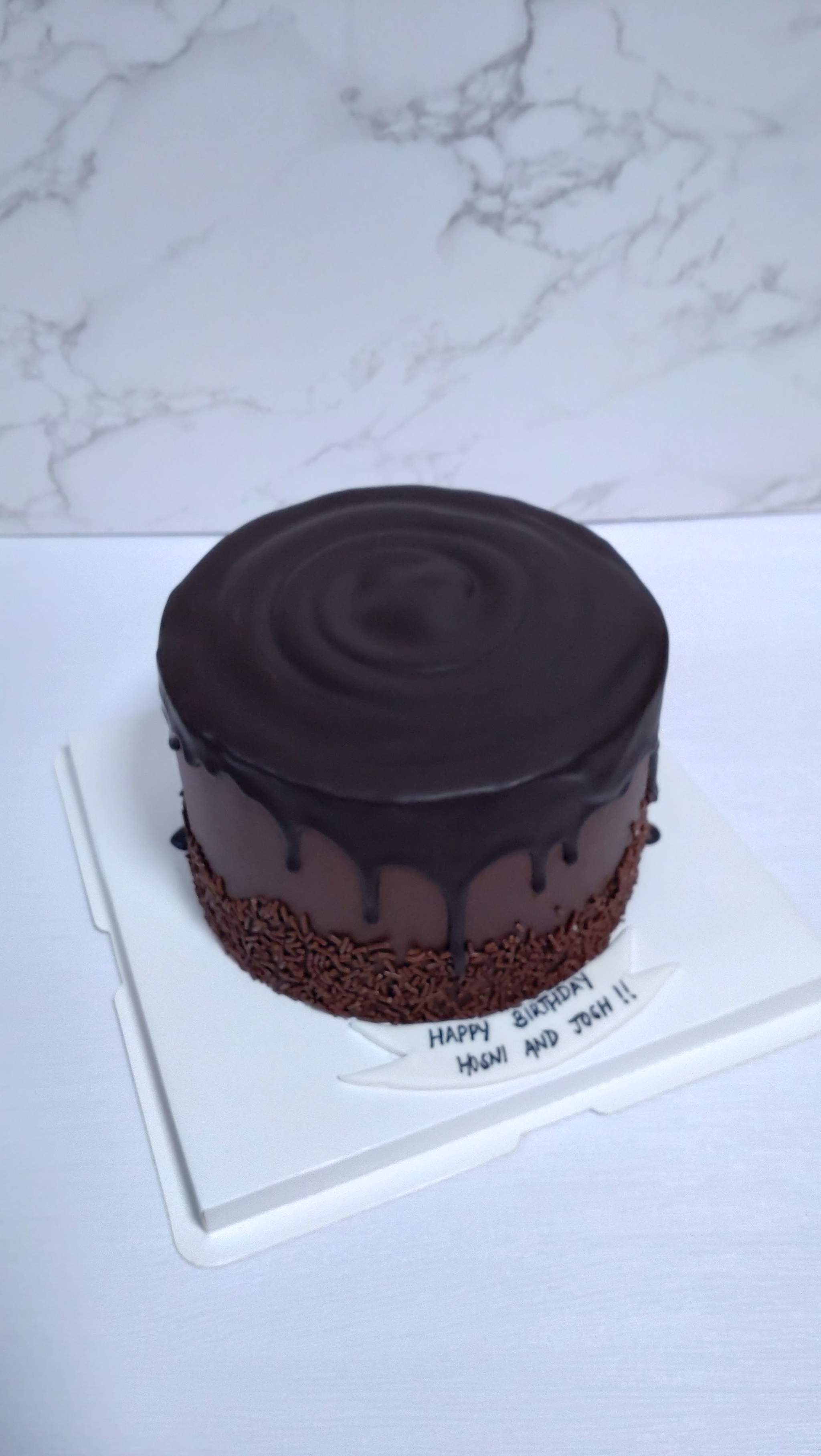 A chocolate drip cake with sprinkles and a birthday banner, by Bakelicious By Aisha.