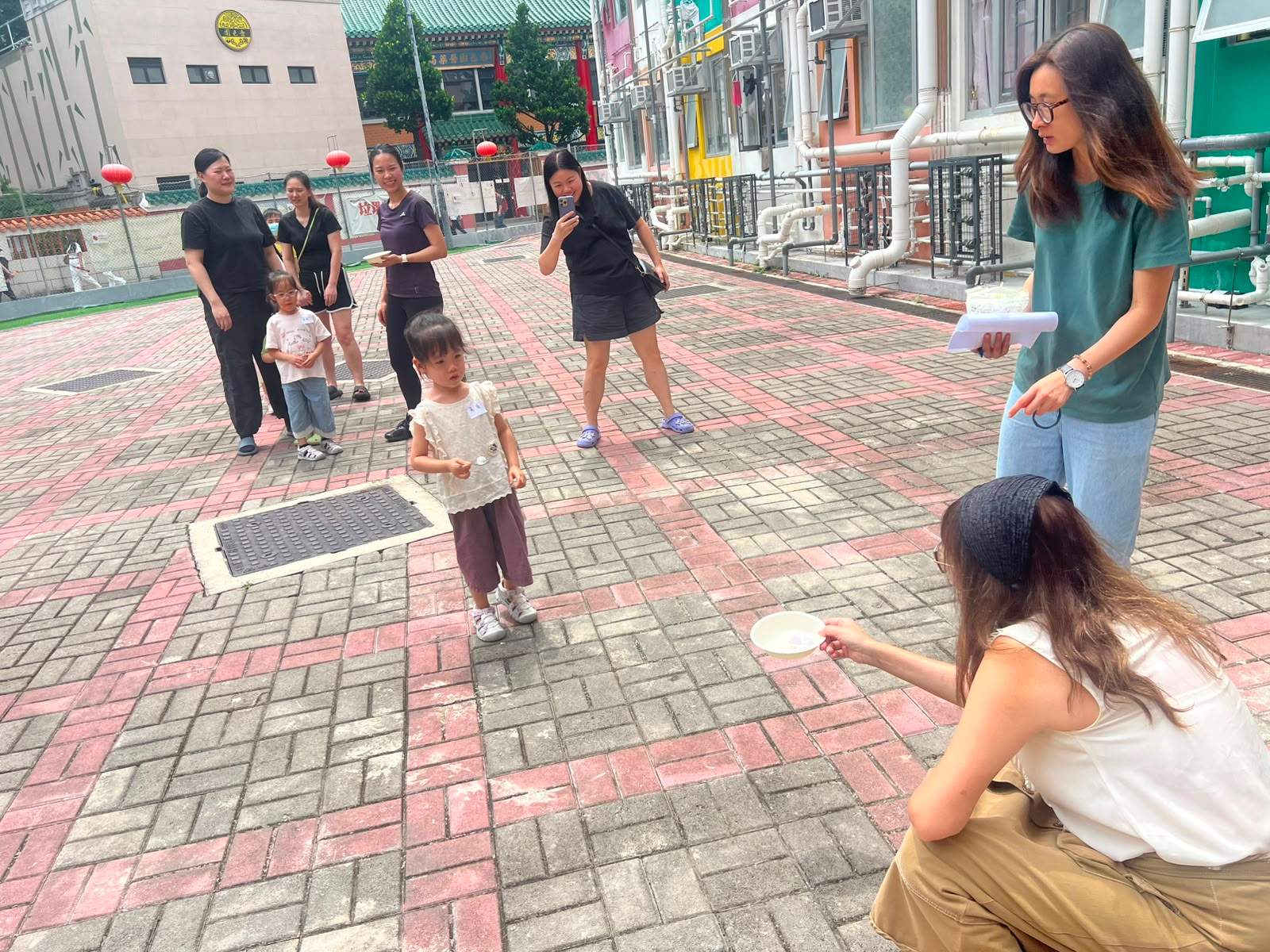 Children and adults play a throwing game in a courtyard.