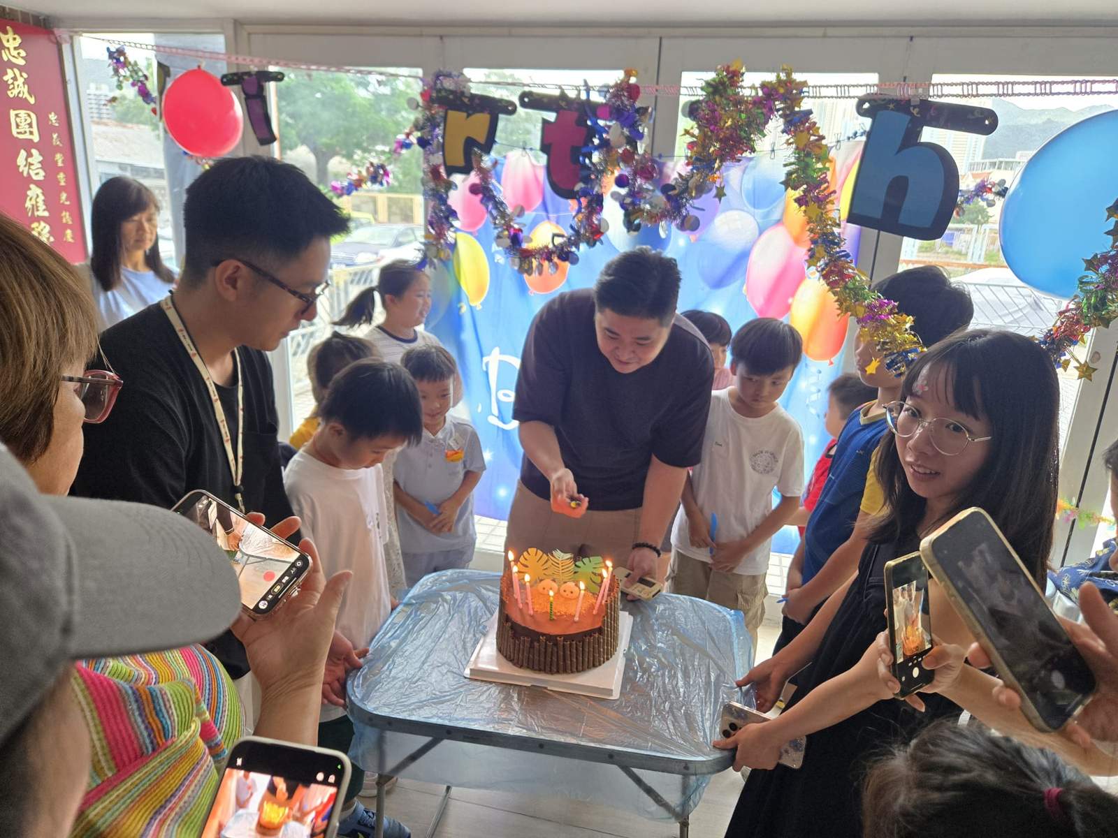 Adults and children gather closely around the candlelit cake.