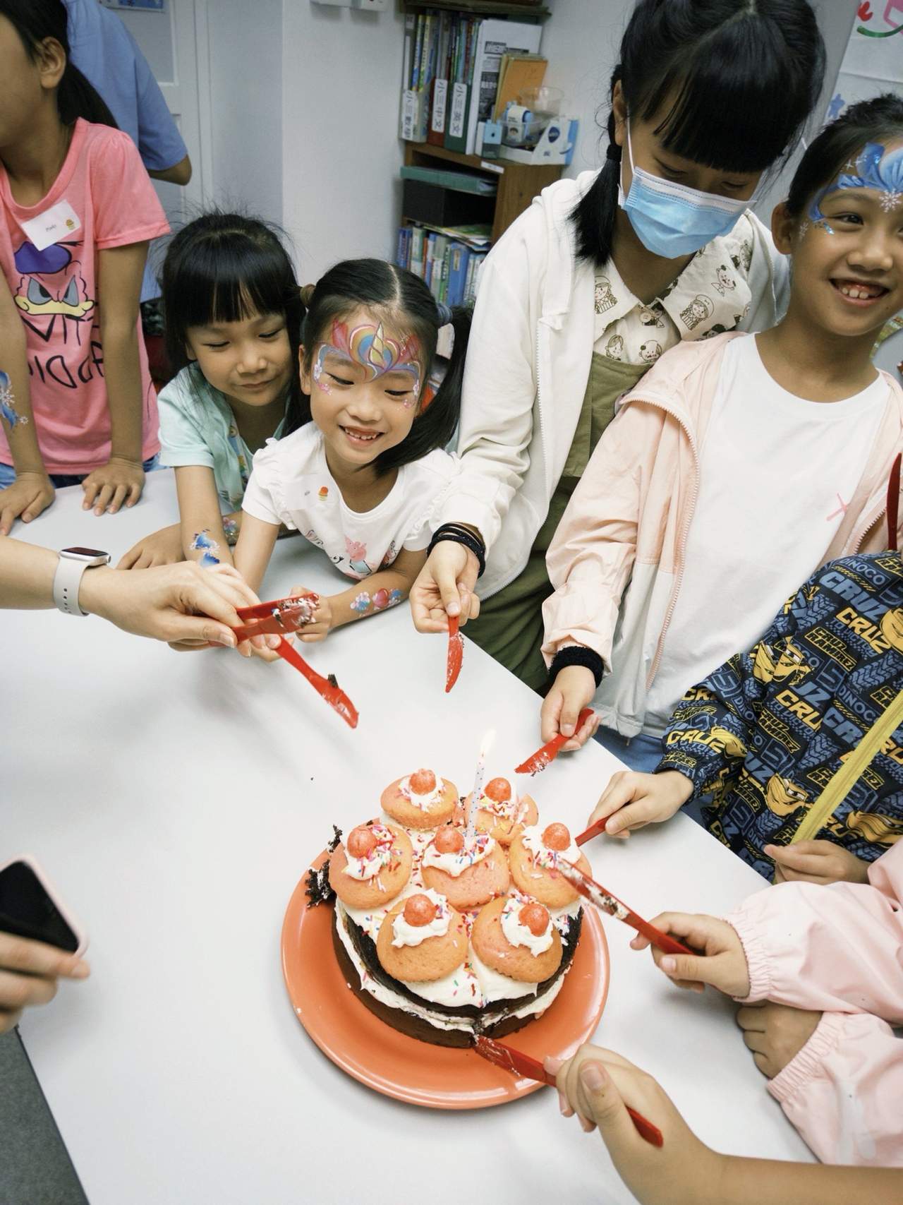 Children gather around cupcakes arranged on a cake stand.