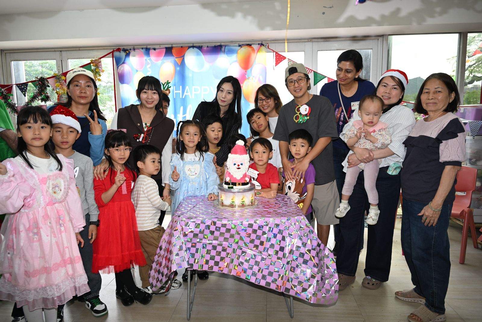 Children and adults pose together around a festive cake table.