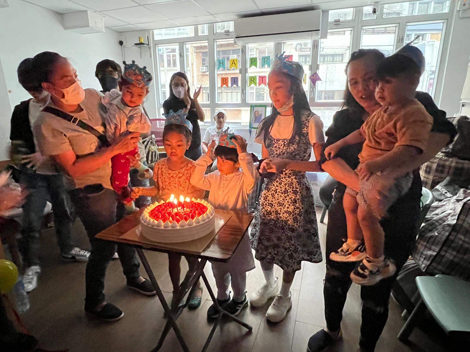 Children and adults gather closely around a cake with lit candles.