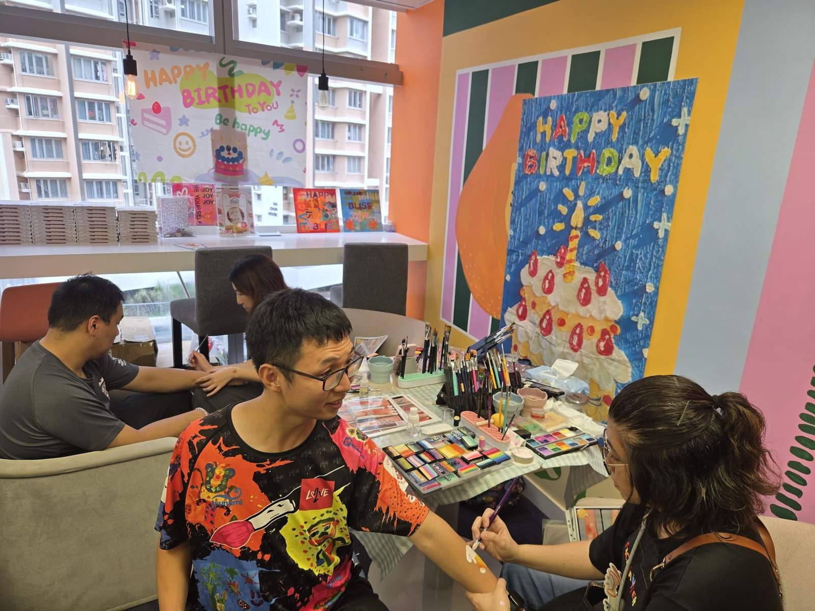 An artist paints a participant’s face beside the birthday display.