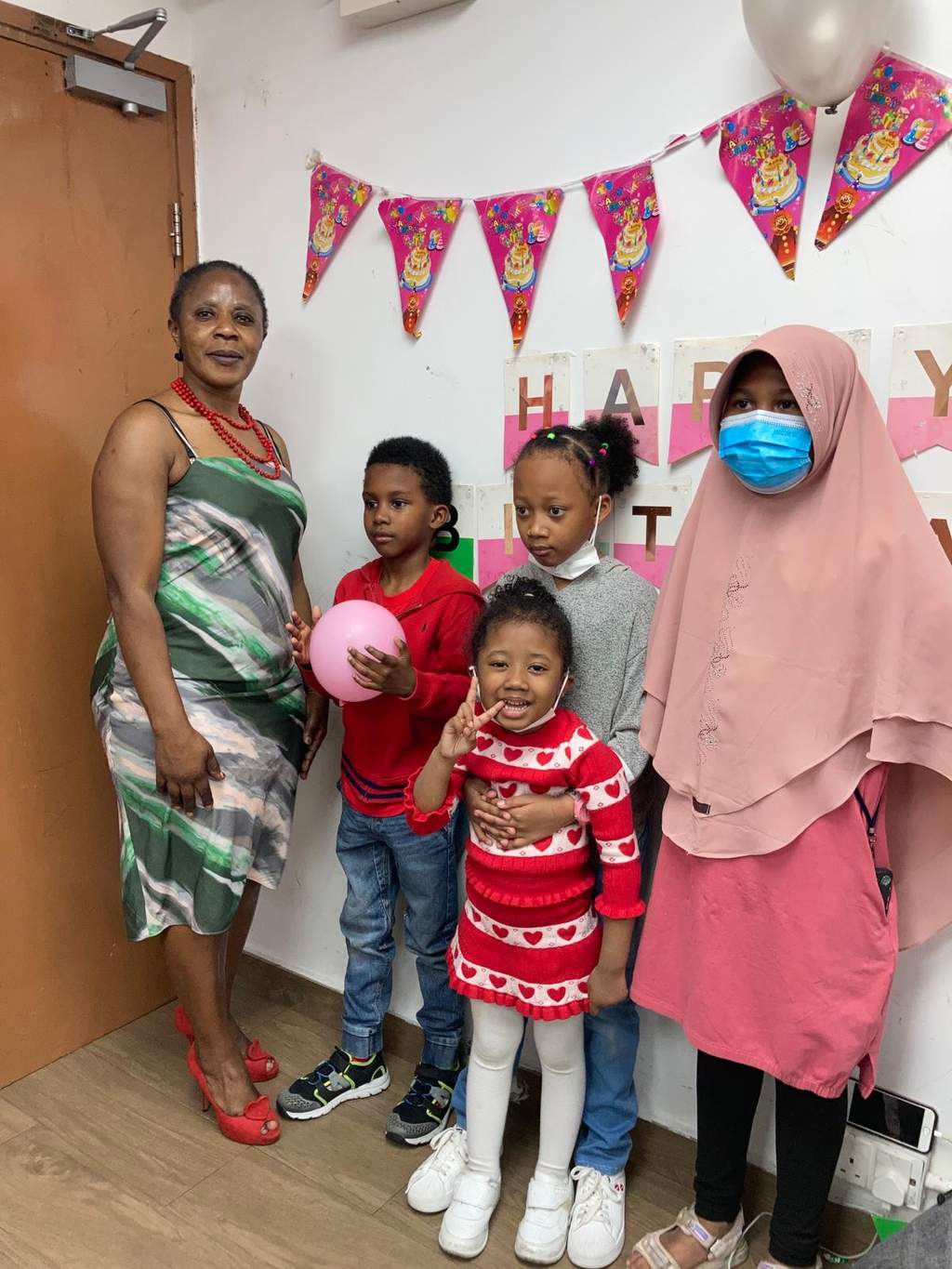 Adults and children pose together with balloons beneath colourful bunting.