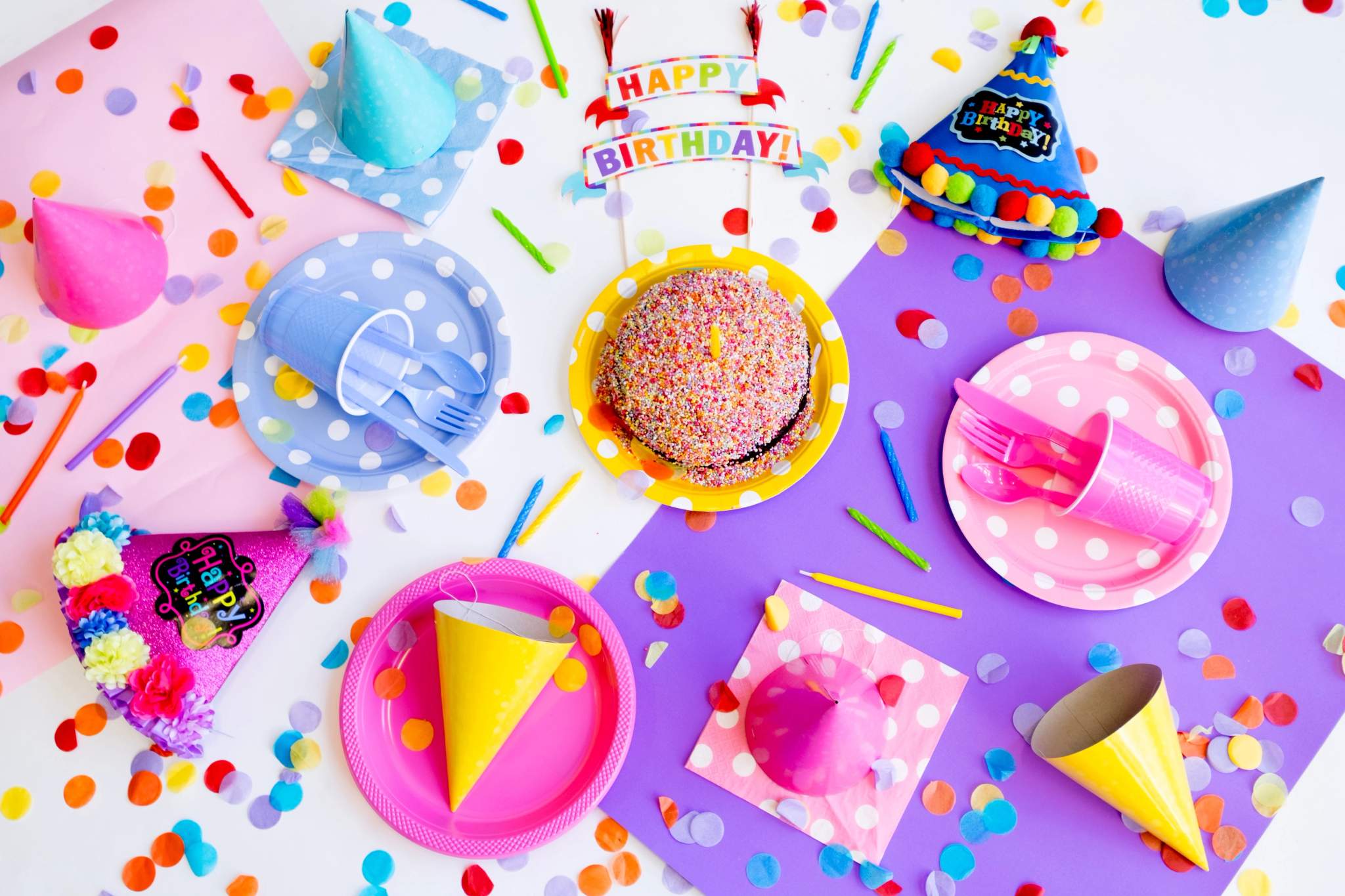A colourful party table displays cake, plates, hats, and scattered confetti.