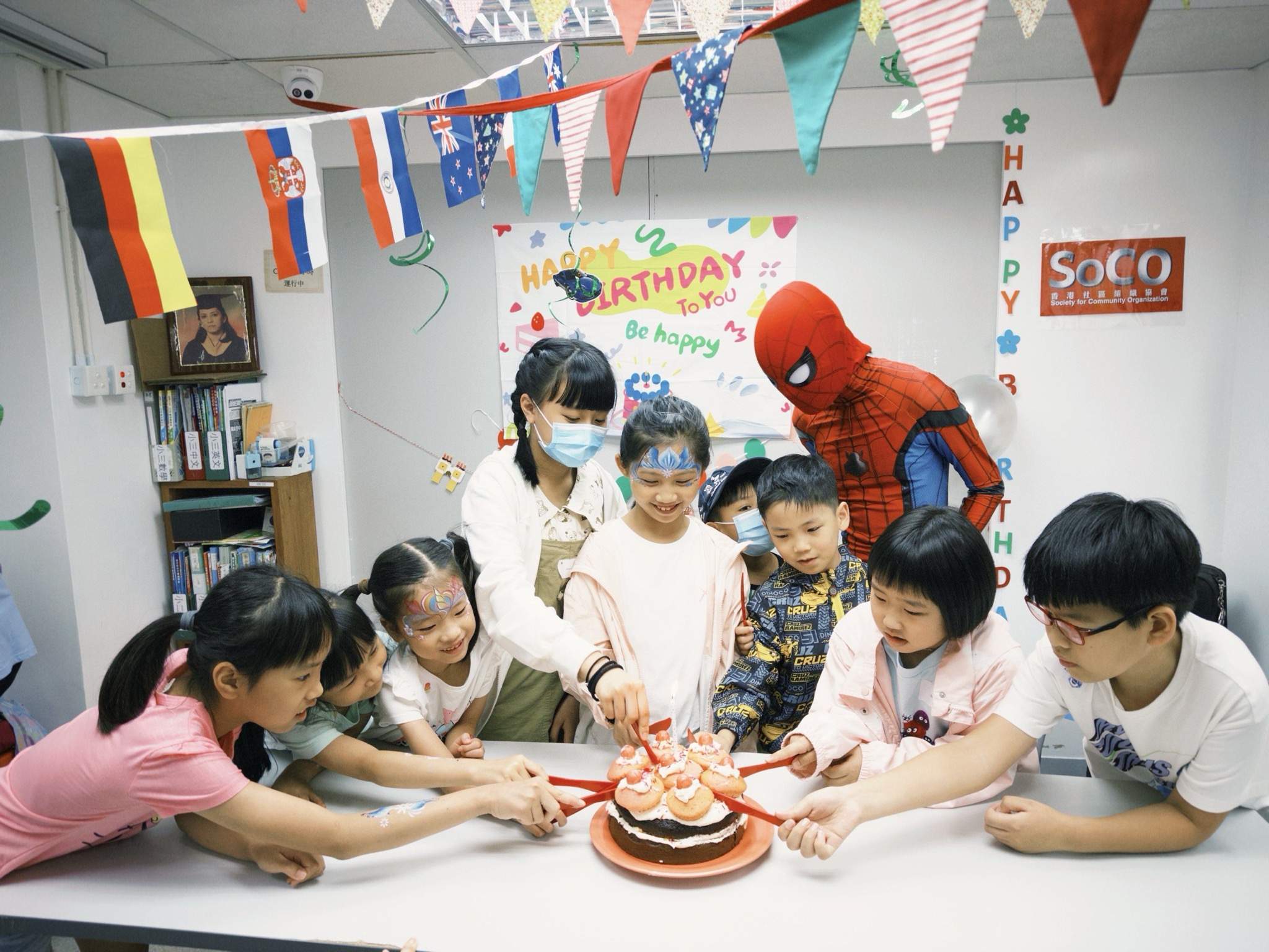 Children reach towards a cake while adults supervise.