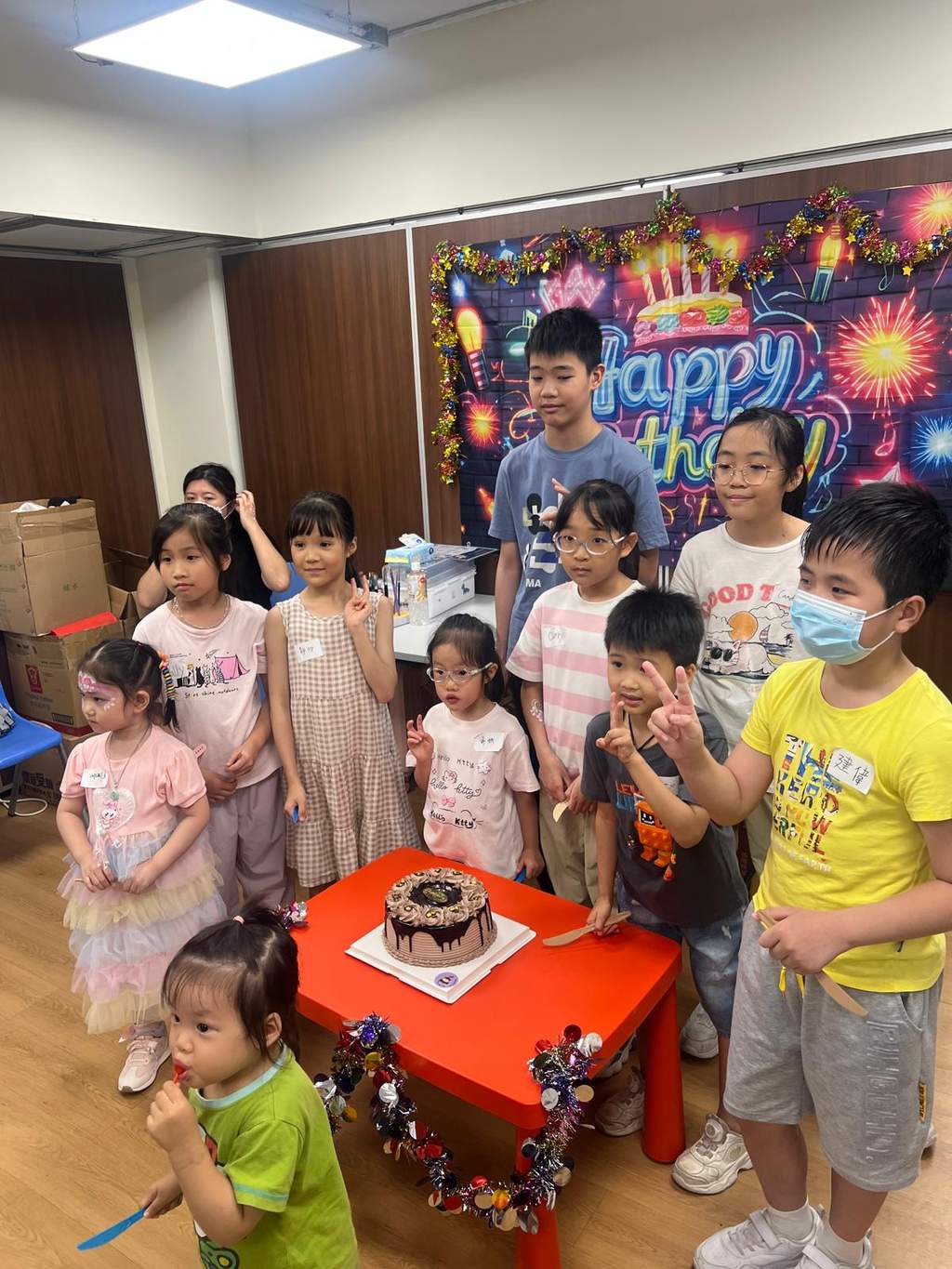 Children stand behind a decorated cake and birthday backdrop.