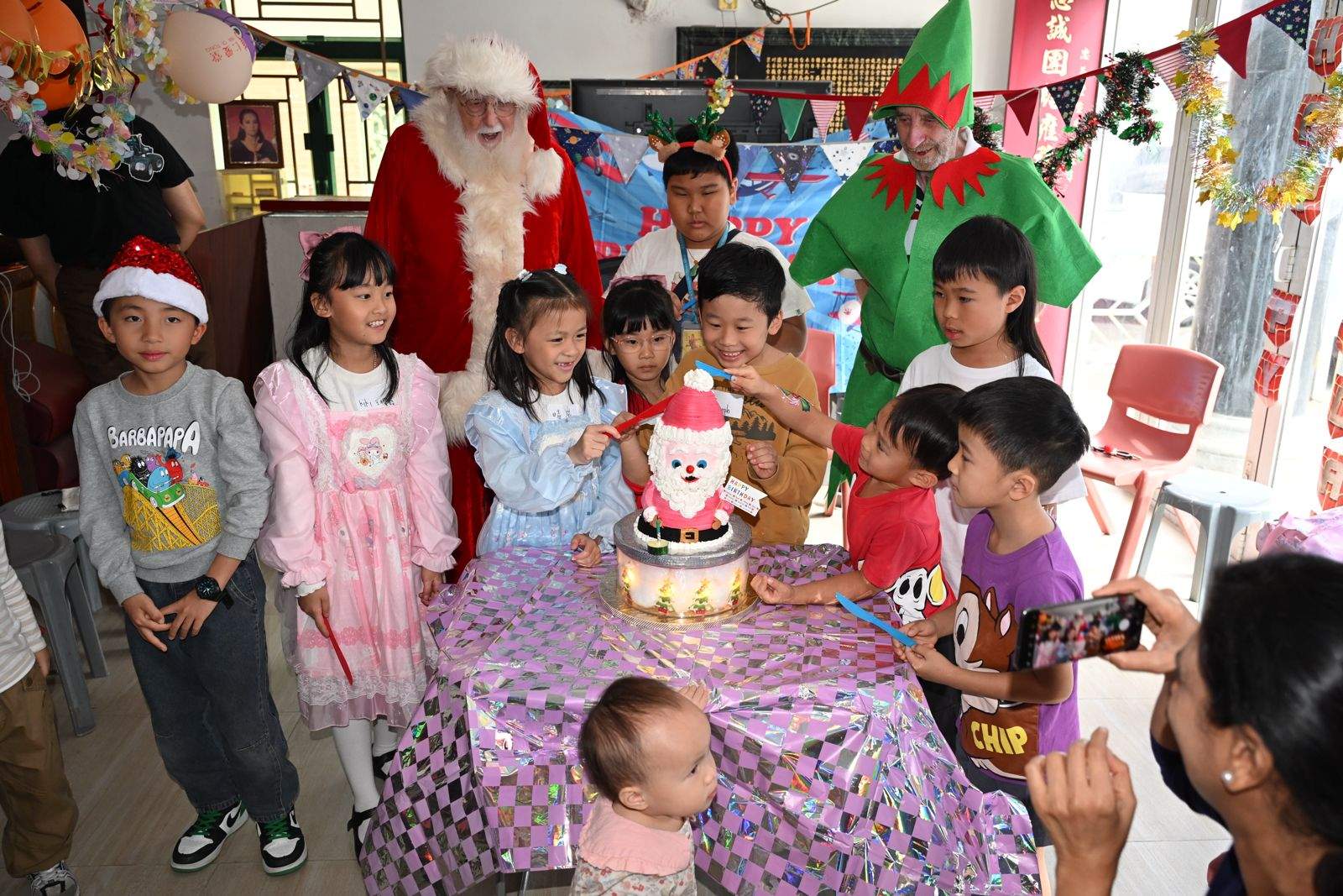 Children gather around a festive cake with two costumed adults.
