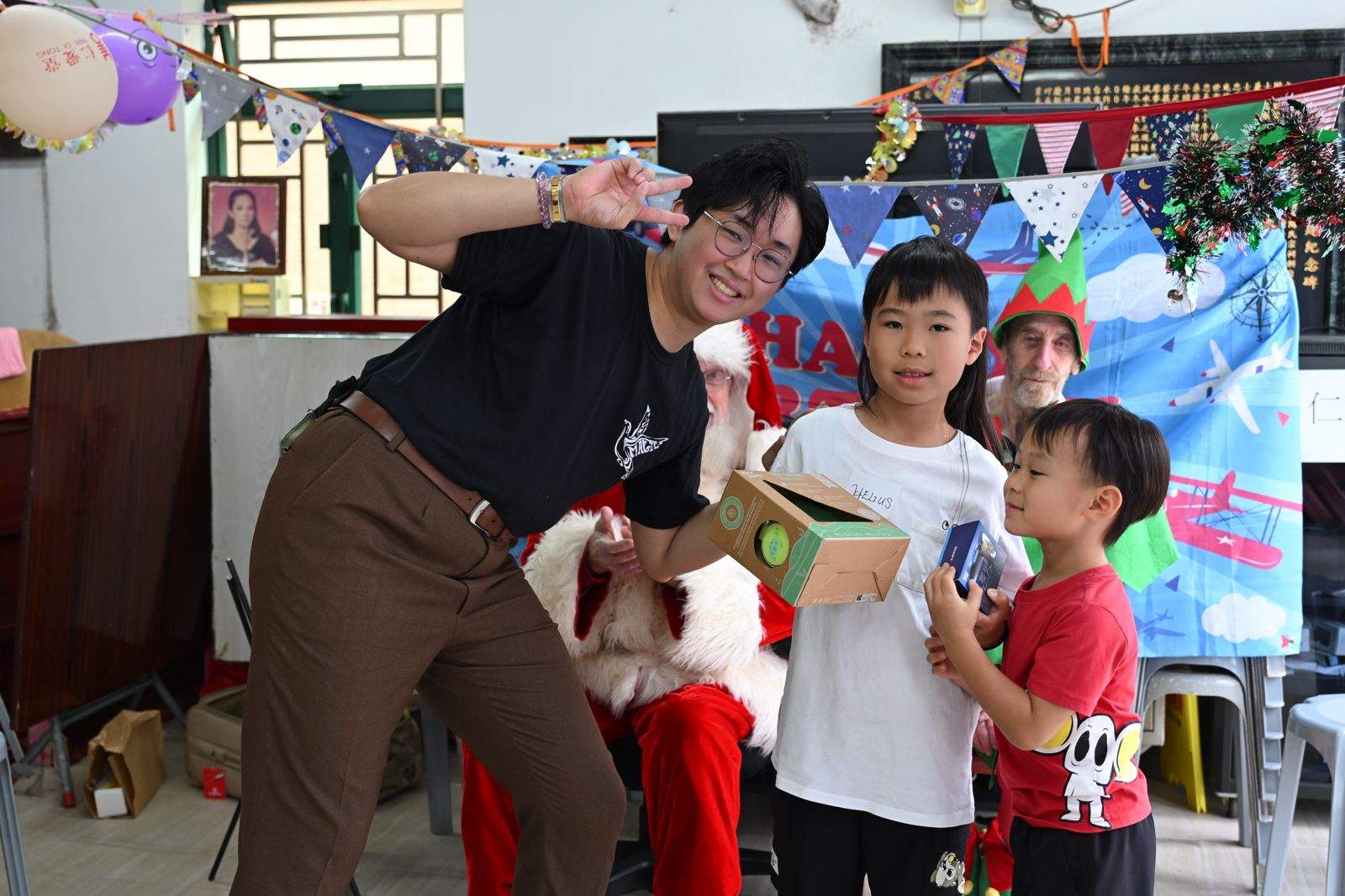 An adult poses beside two children holding a gift box.