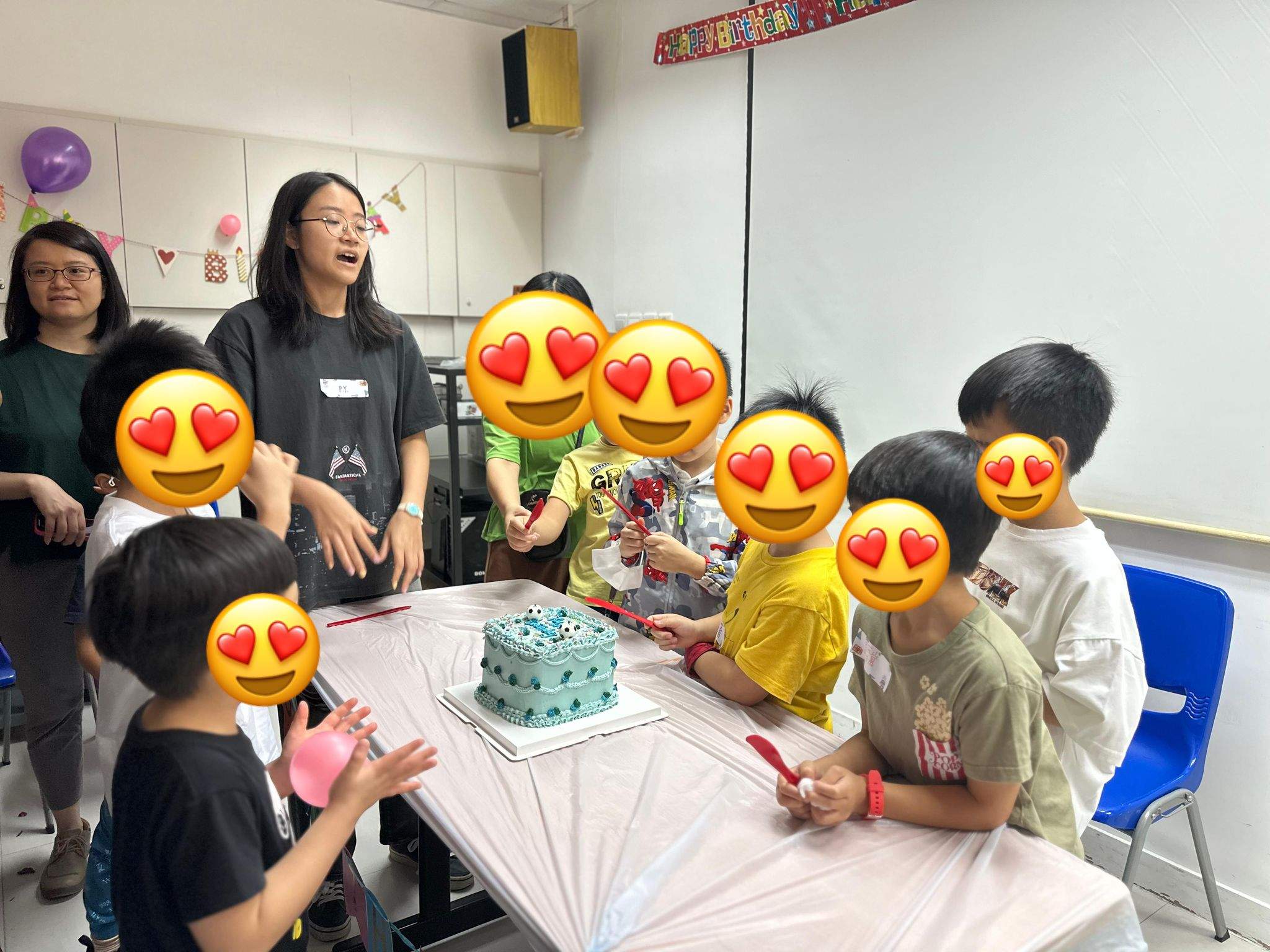 Children crowd around a cake while adults stand behind them.