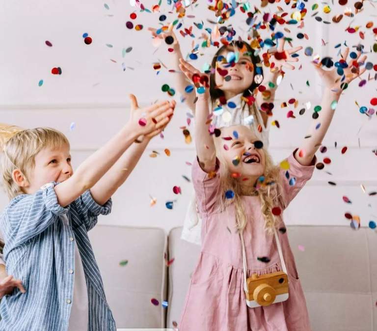 Three children toss colourful confetti into the air together.