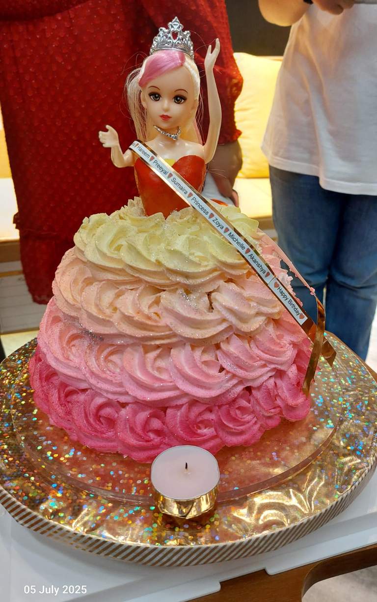 A pink doll-shaped cake stands decorated with swirled frosting.