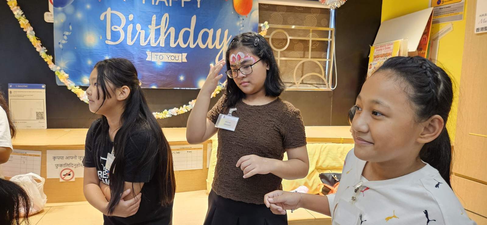 Three children stand together in front of the birthday backdrop.