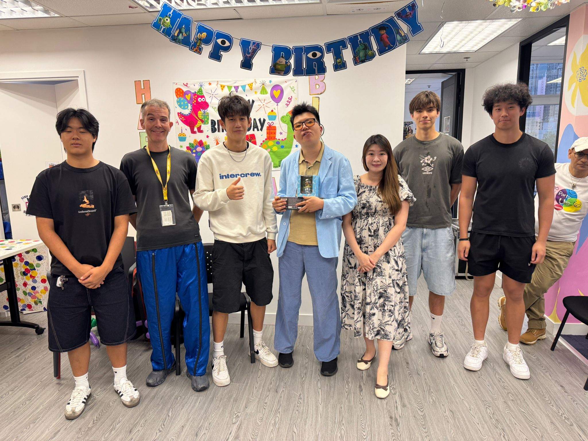Six people pose together beneath hanging birthday decorations.