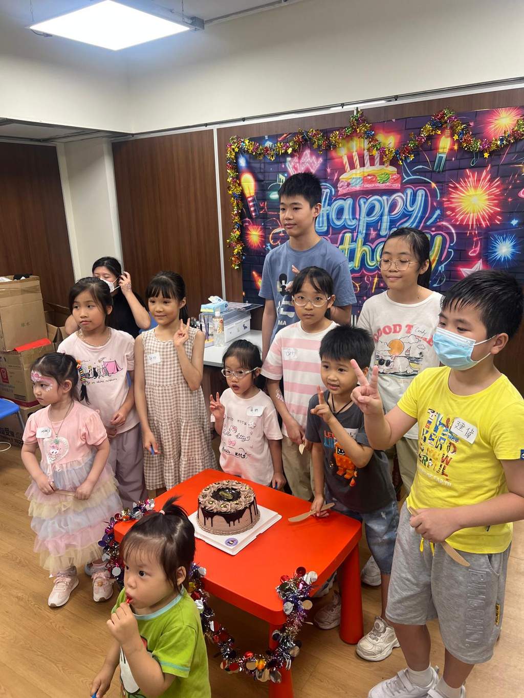 Children gather around a cake on a small red table.
