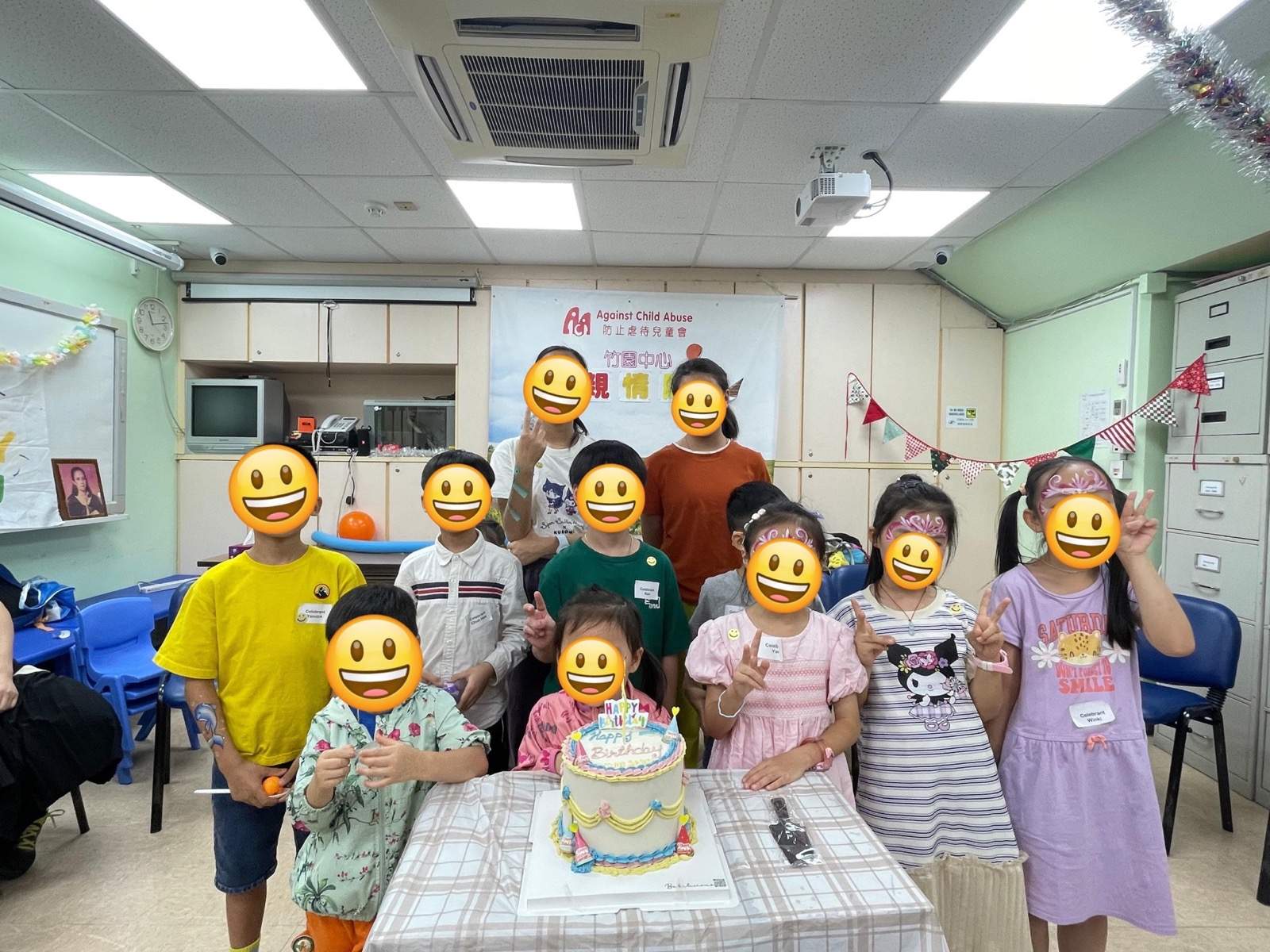 Children gather behind a decorated cake on a table.
