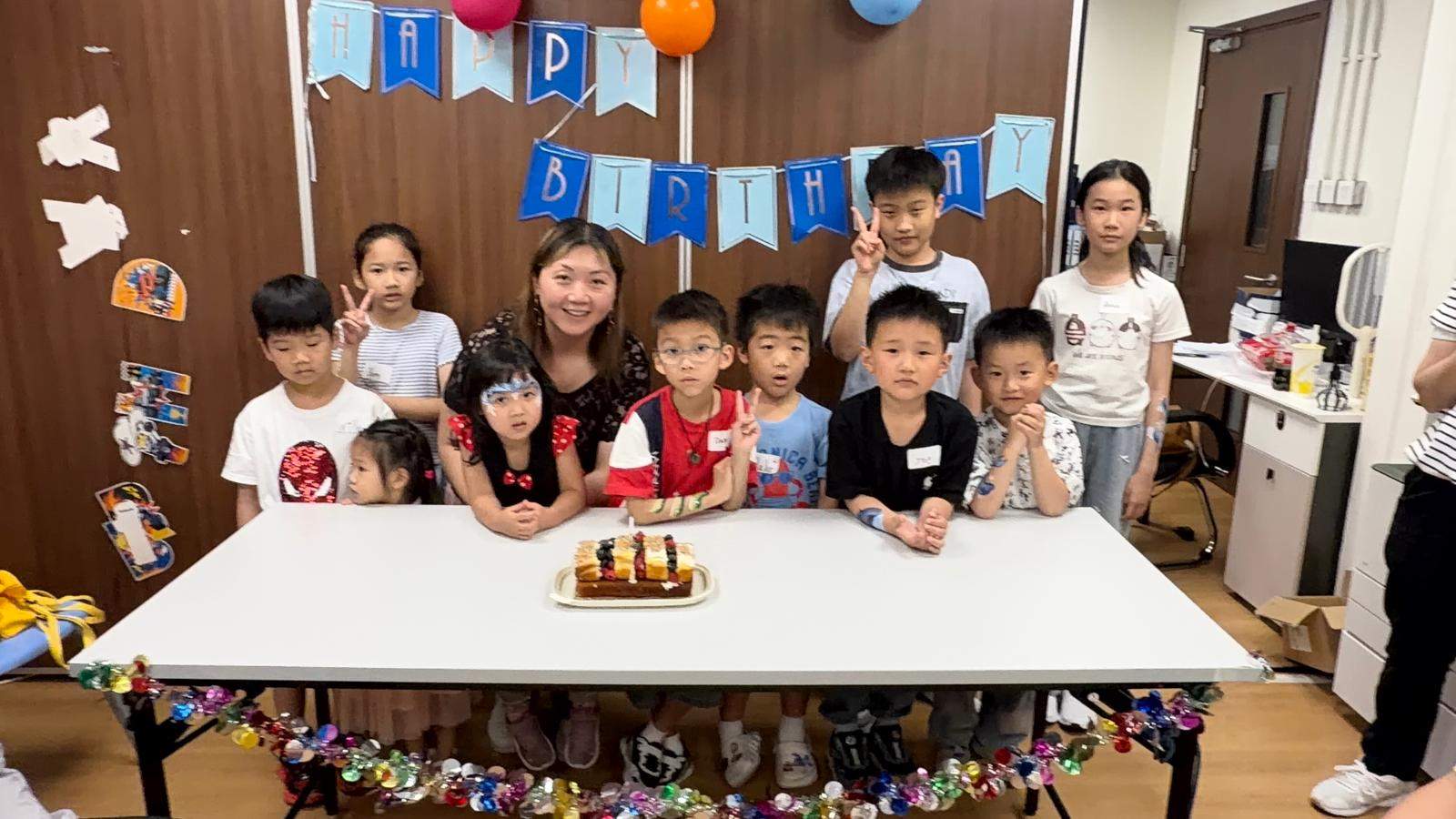 Children and adults pose behind a small cake on a table.