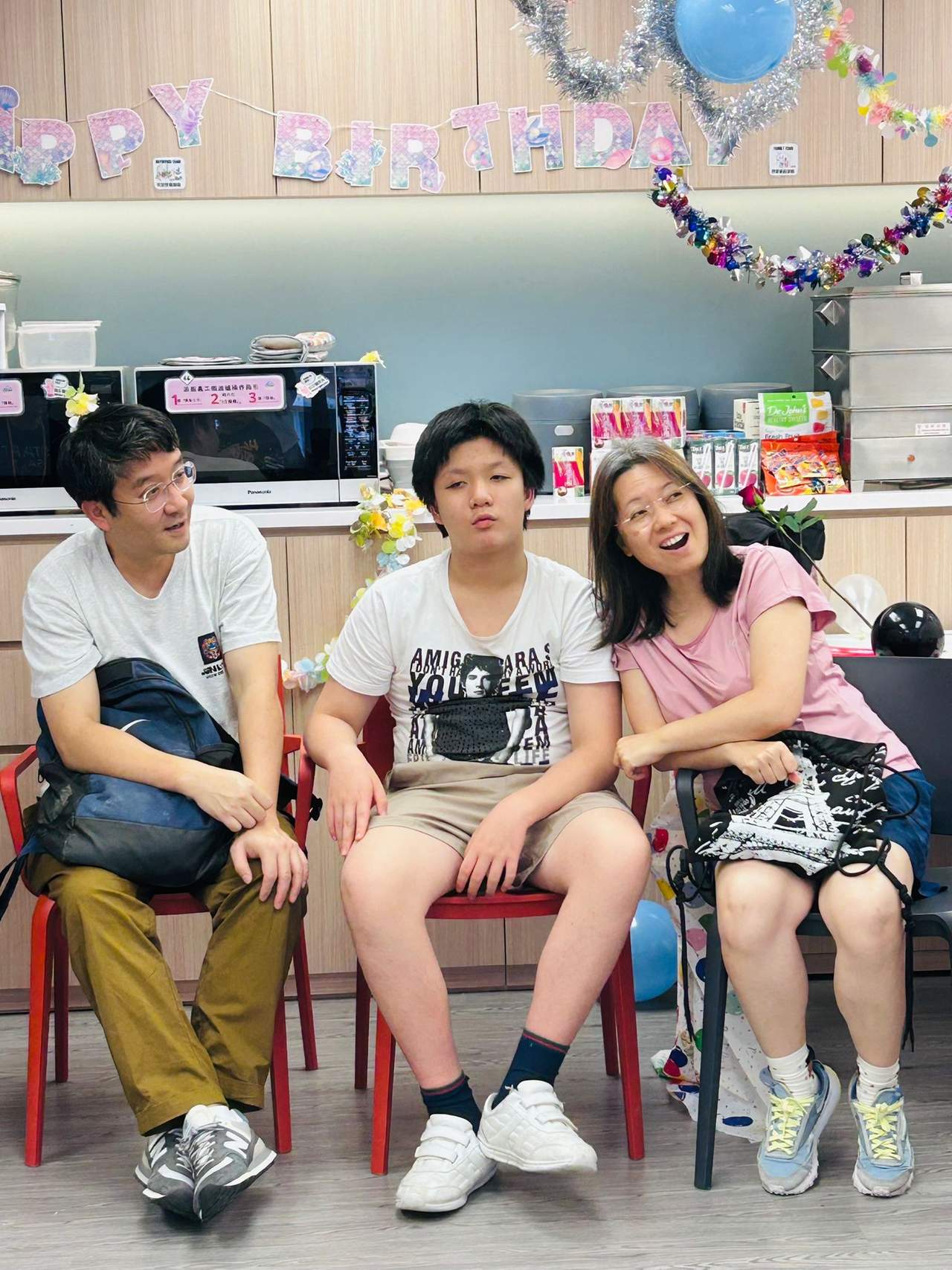 Three people sit together on chairs beneath hanging decorations.