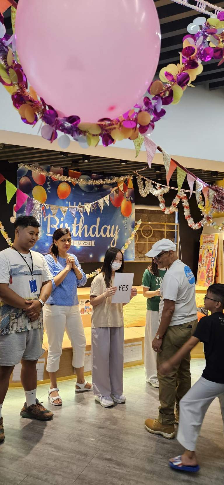Children and adults stand beneath a large balloon near the backdrop.