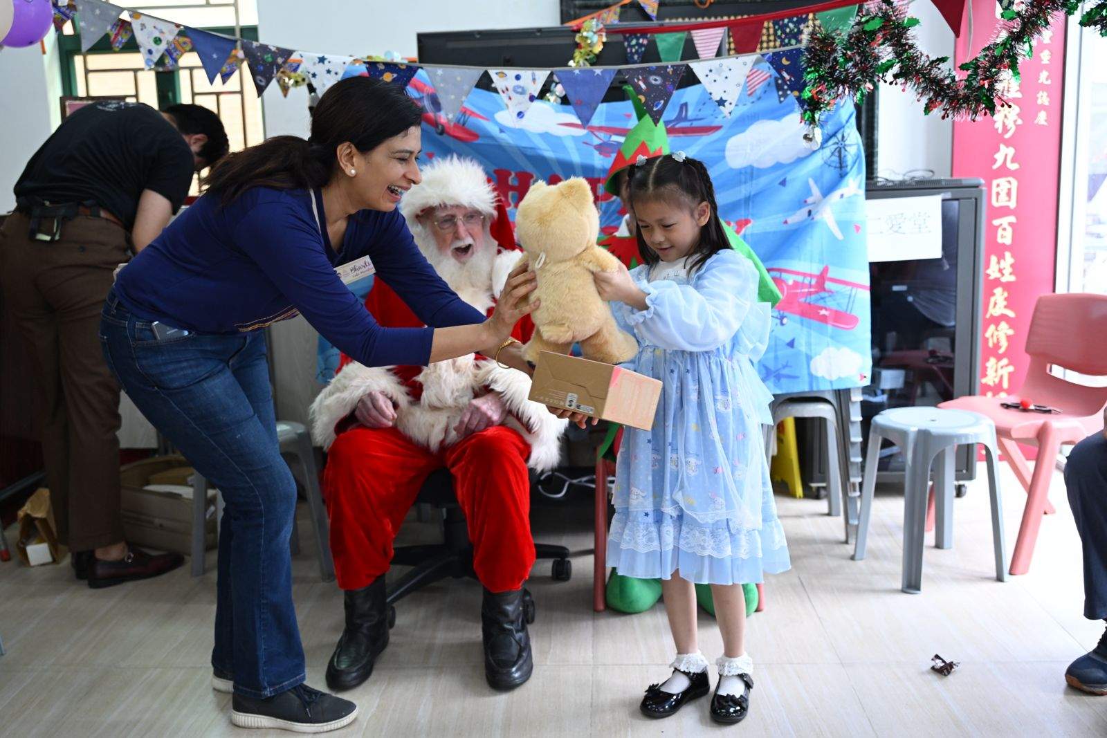 An adult helps a child receive a gift from a costumed adult.