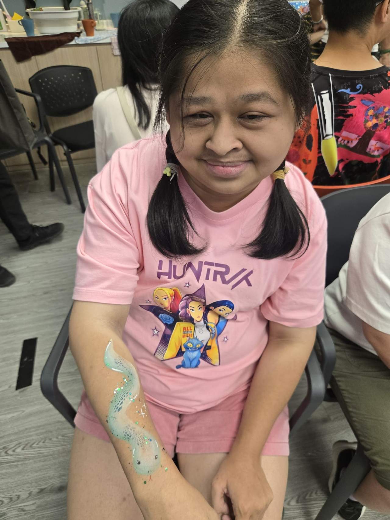 A participant smiles while showing colourful paint on both arms.