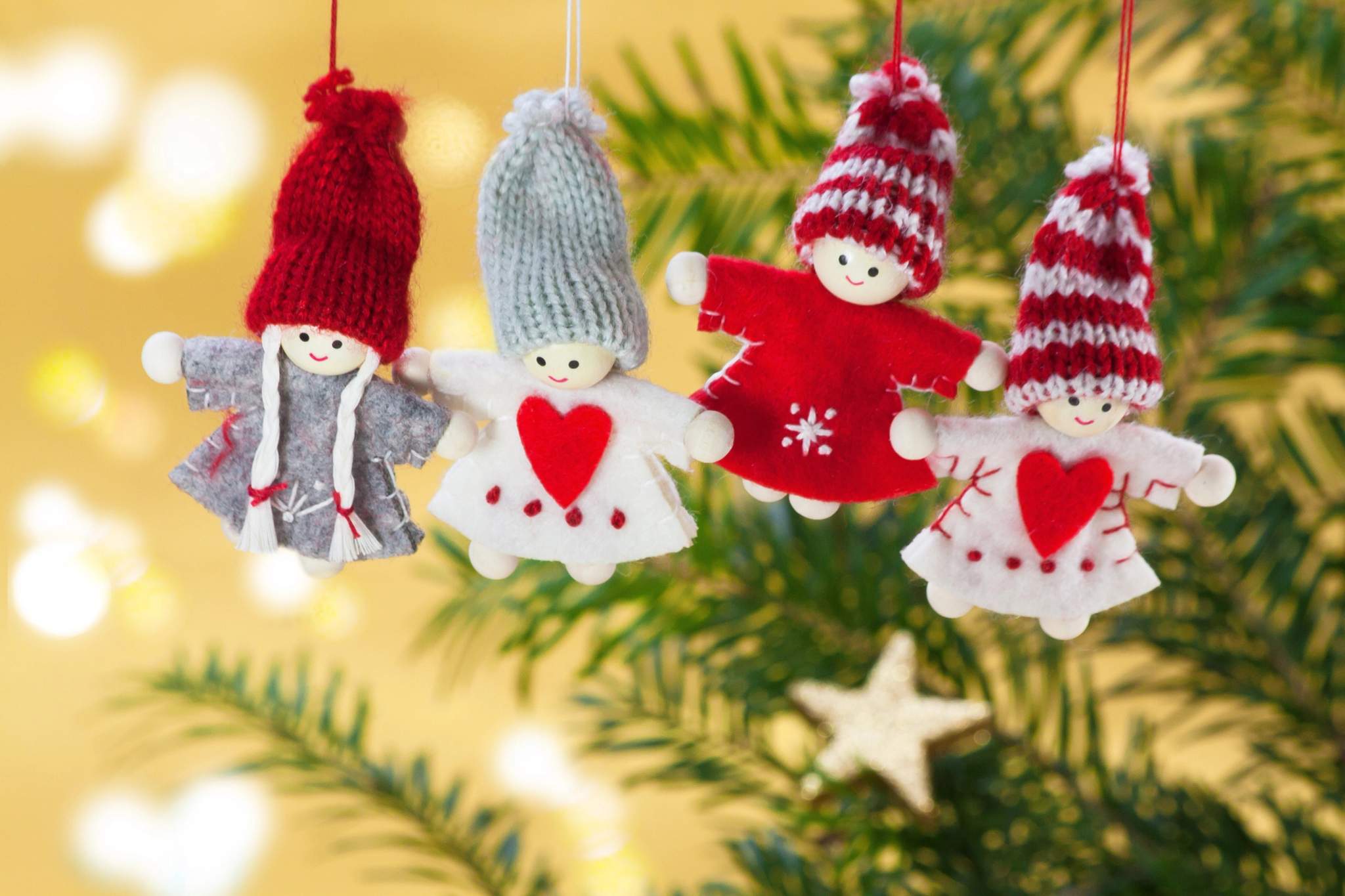 Four felt ornaments hang from an illuminated evergreen branch.