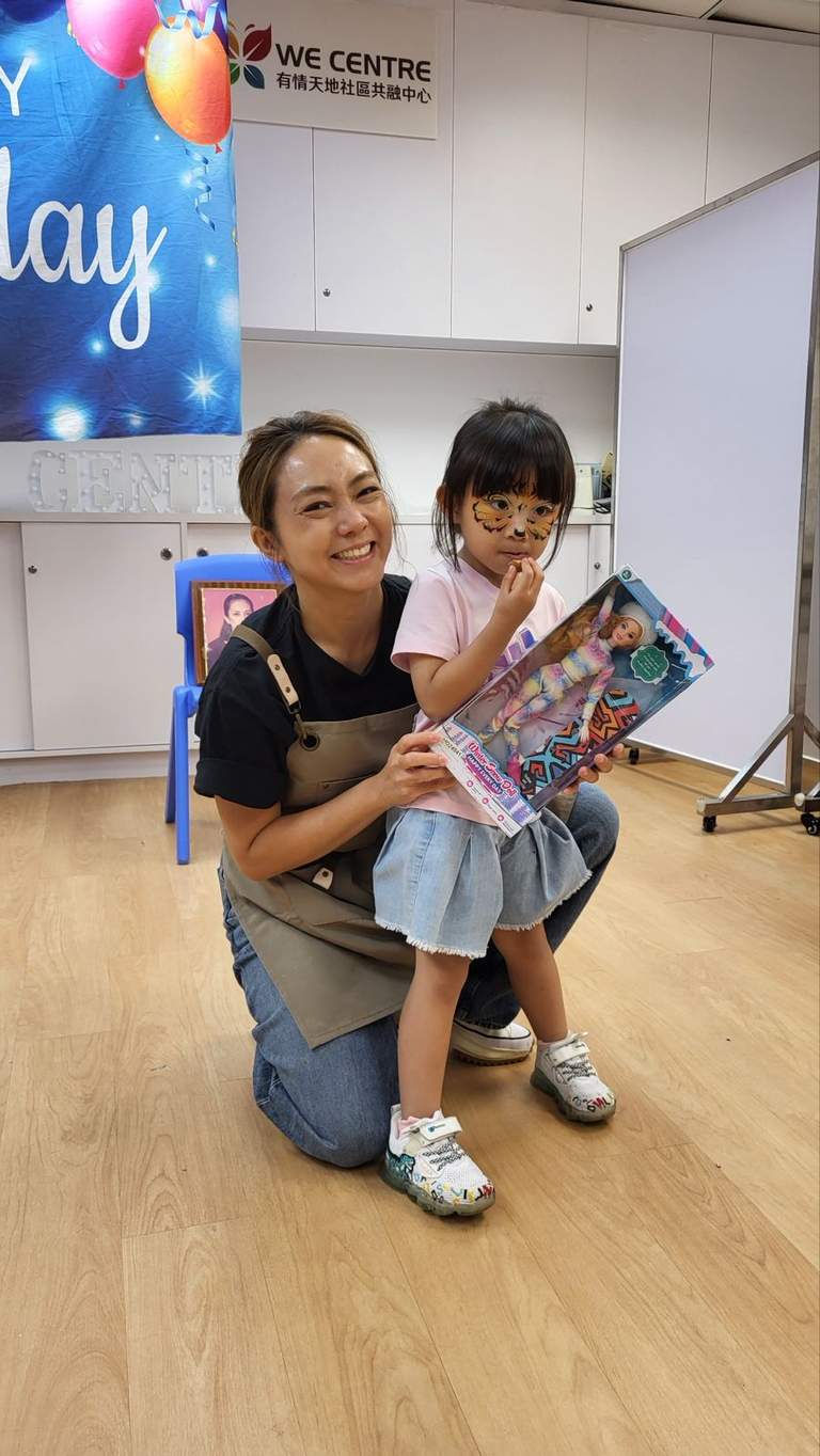 An adult kneels beside a child holding a wrapped gift.