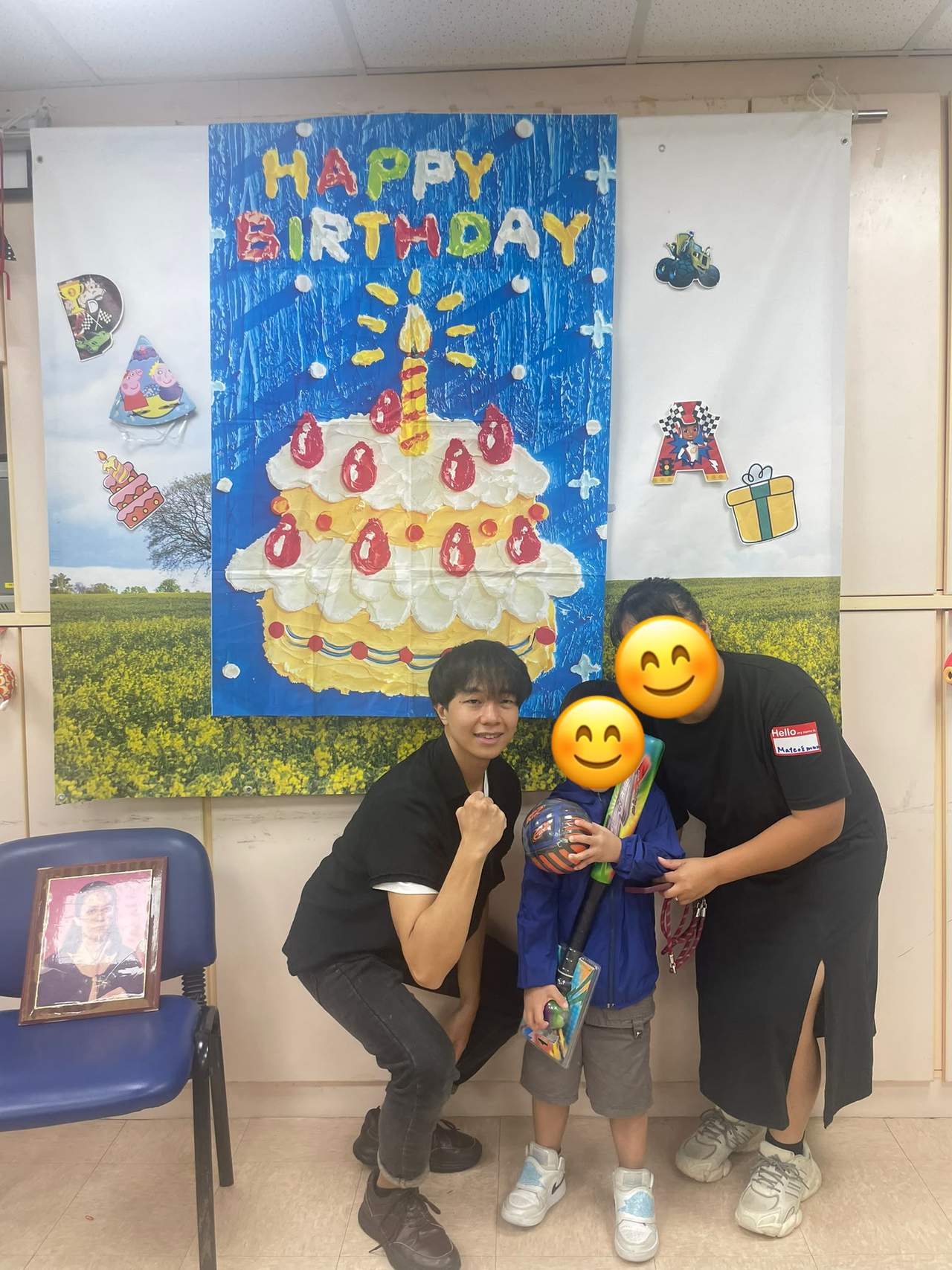 A child receives gifts beside two adults before birthday decorations.