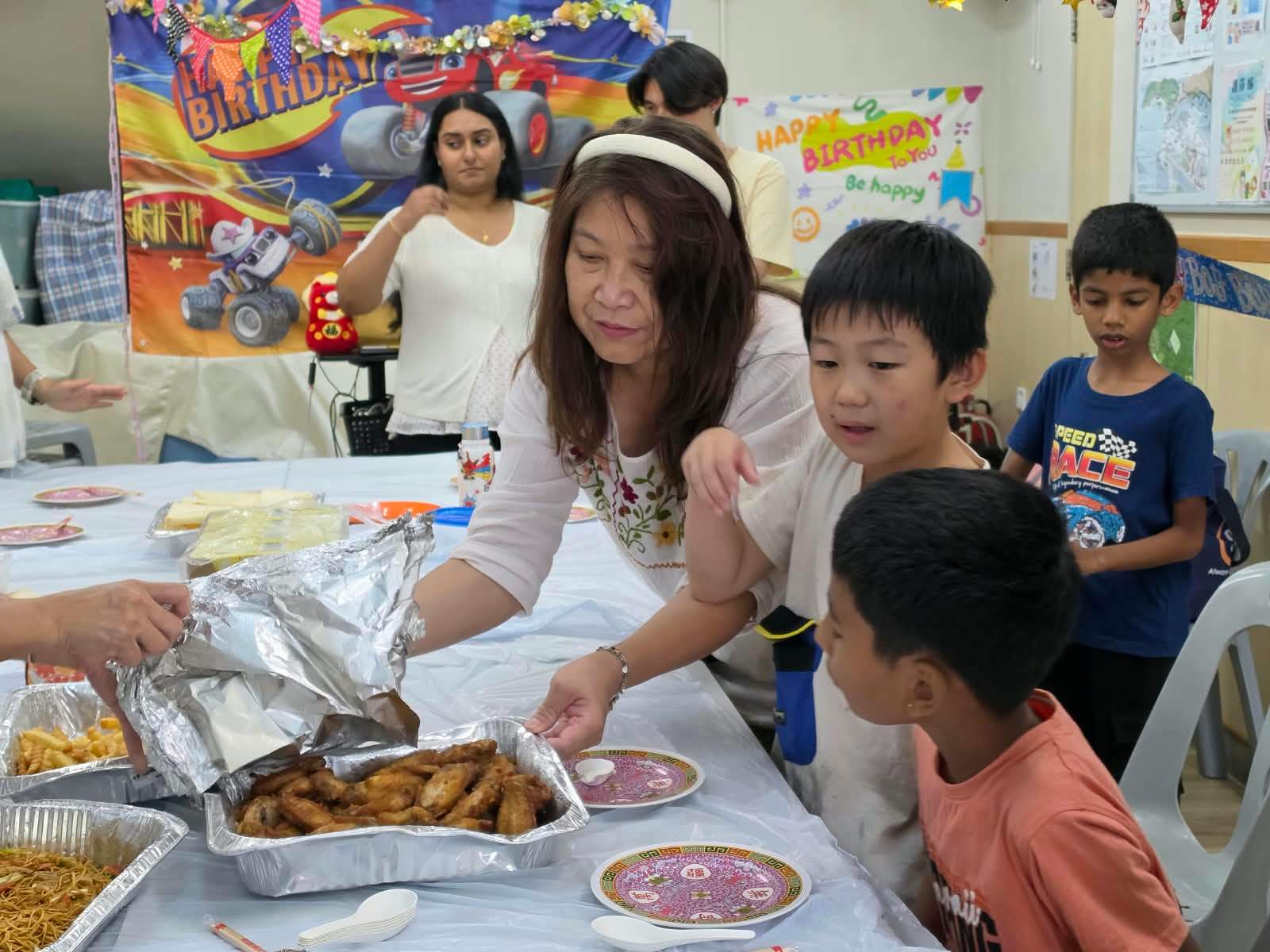 Volunteers serve a shared meal to children around the table.