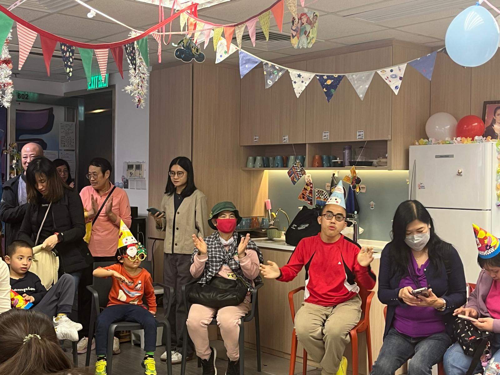 People sit in a semicircle wearing paper party hats.