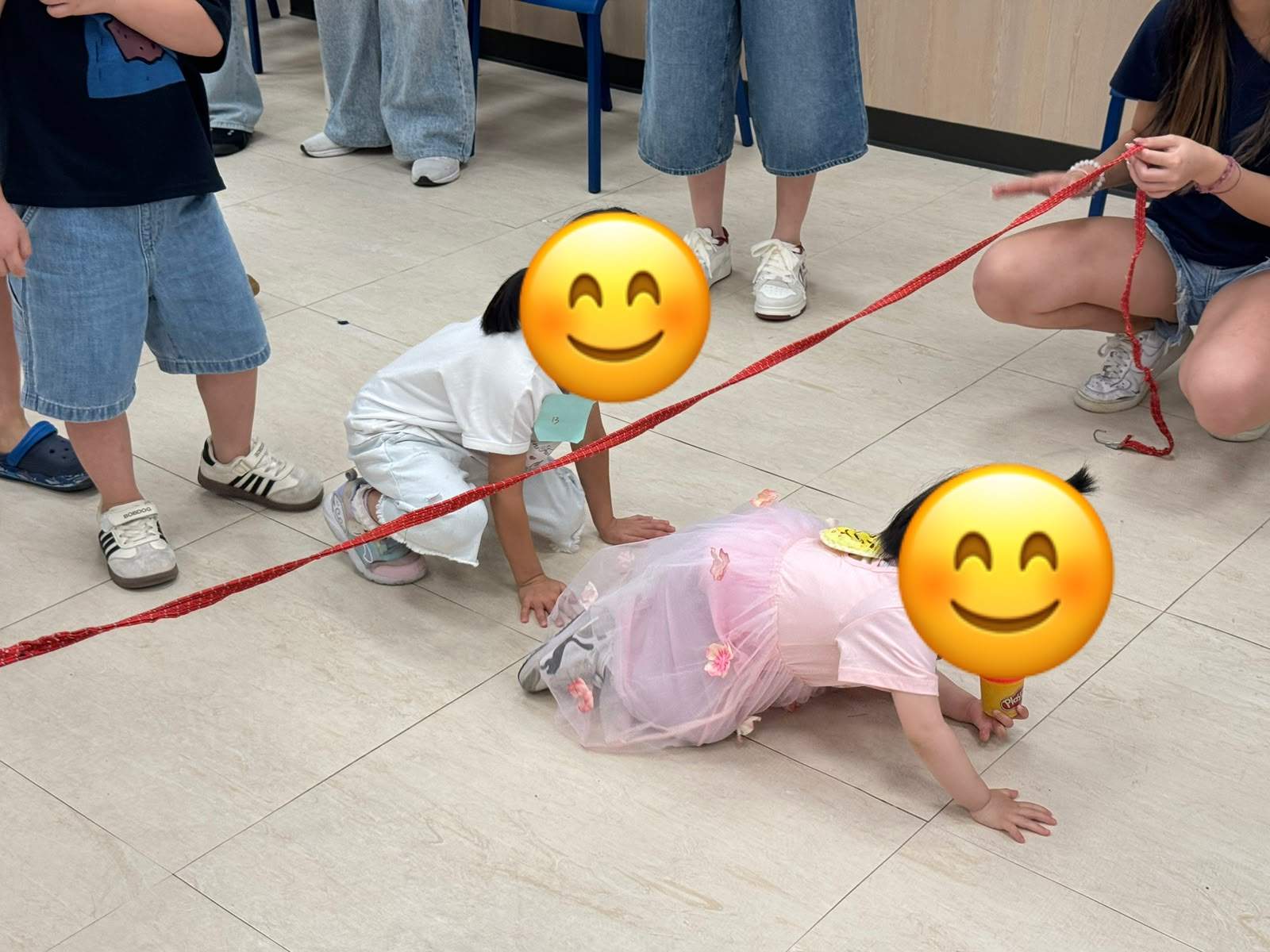 Two children crawl beneath a red rope during a game.