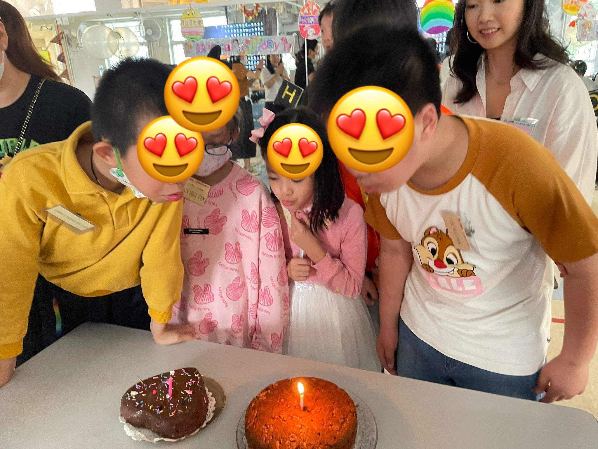 People lean towards two cakes topped with lit candles.