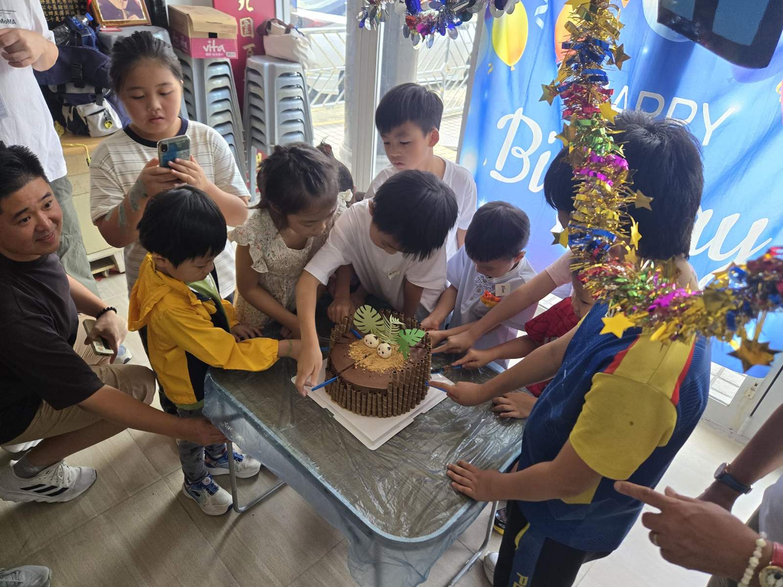 Children and adults reach towards the cake together.