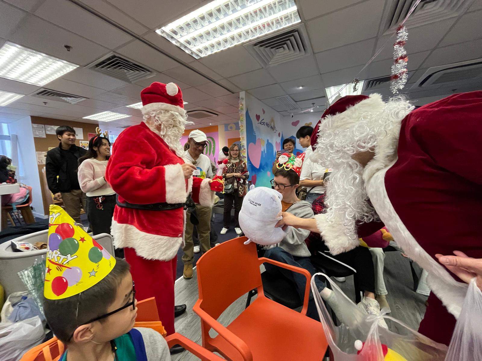 Two costumed adults distribute gifts among seated people.