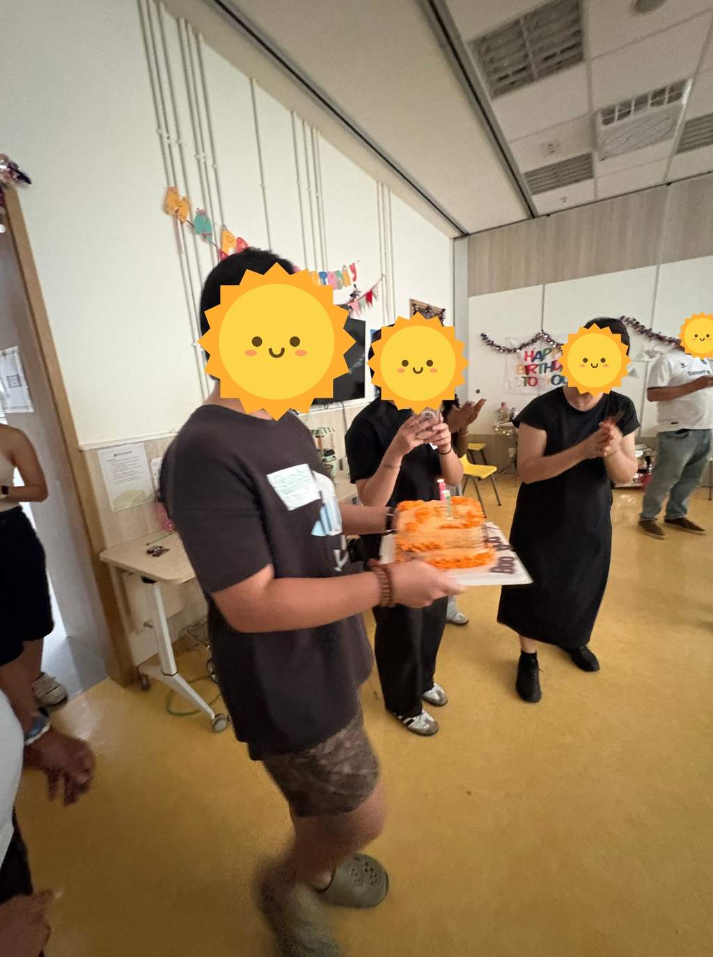 Volunteers carrying a birthday cake and clapping beside birthday decorations.