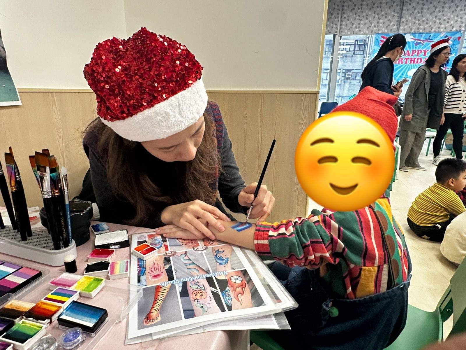 An adult paints a seated child's face at an activity table.