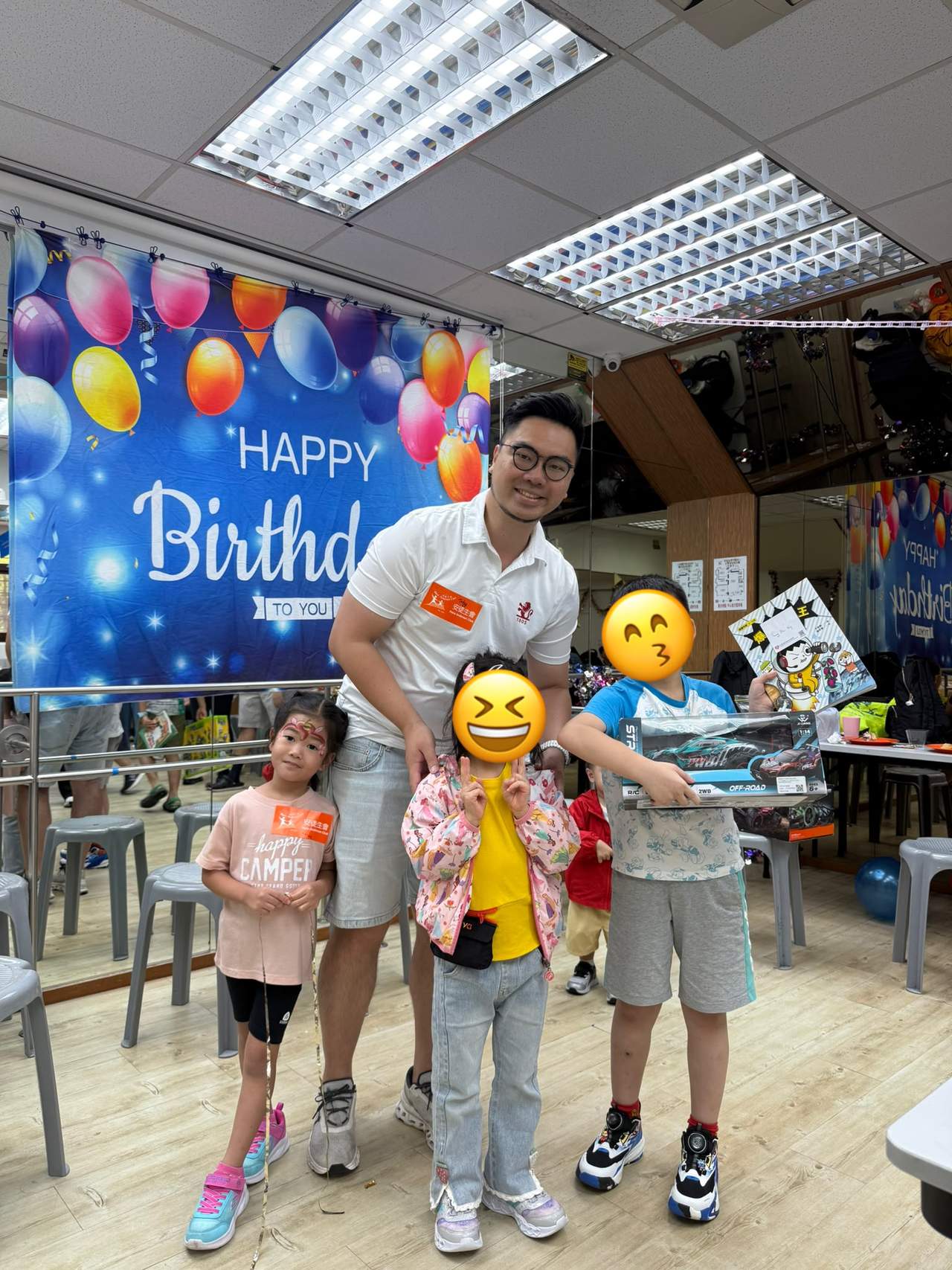An adult stands behind three children holding gifts.