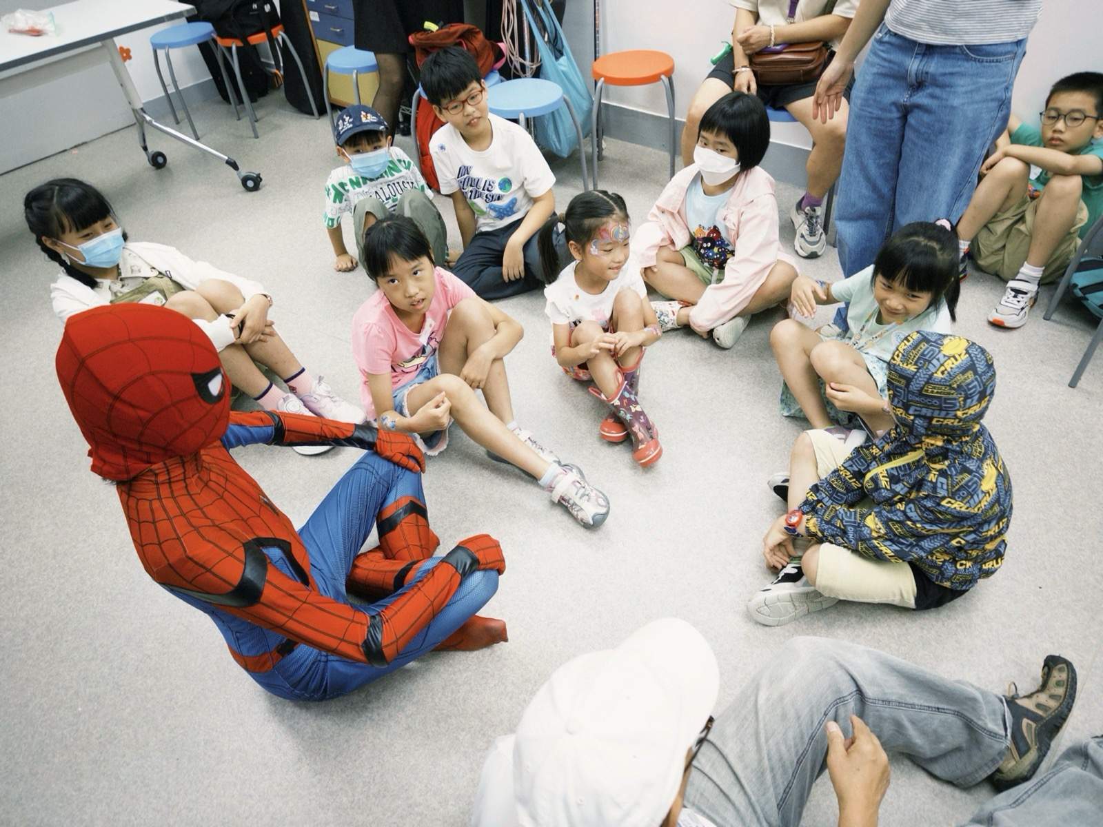 Children sit on the floor around a kneeling costumed performer.