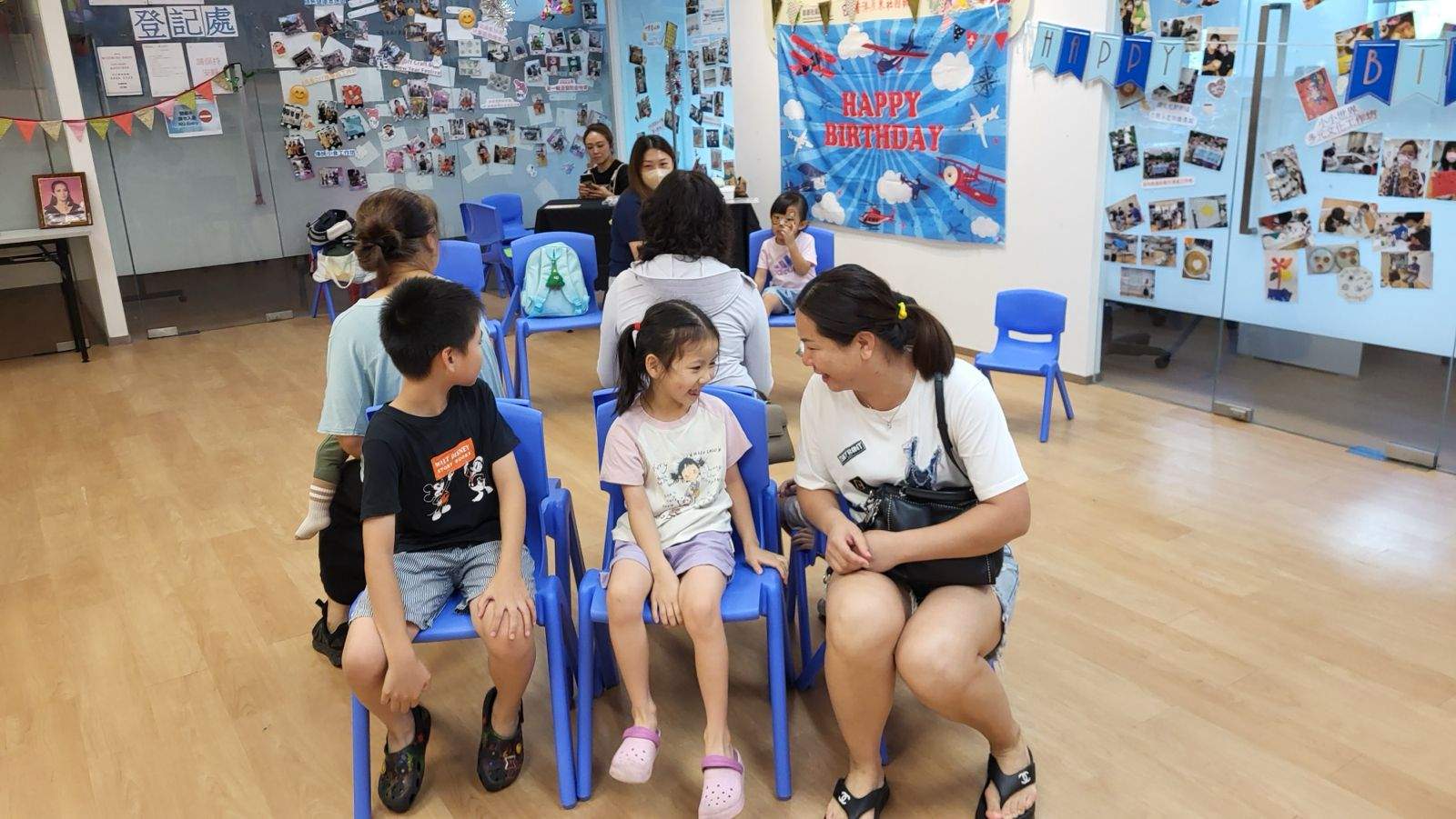 Two children and an adult sit together on blue chairs.
