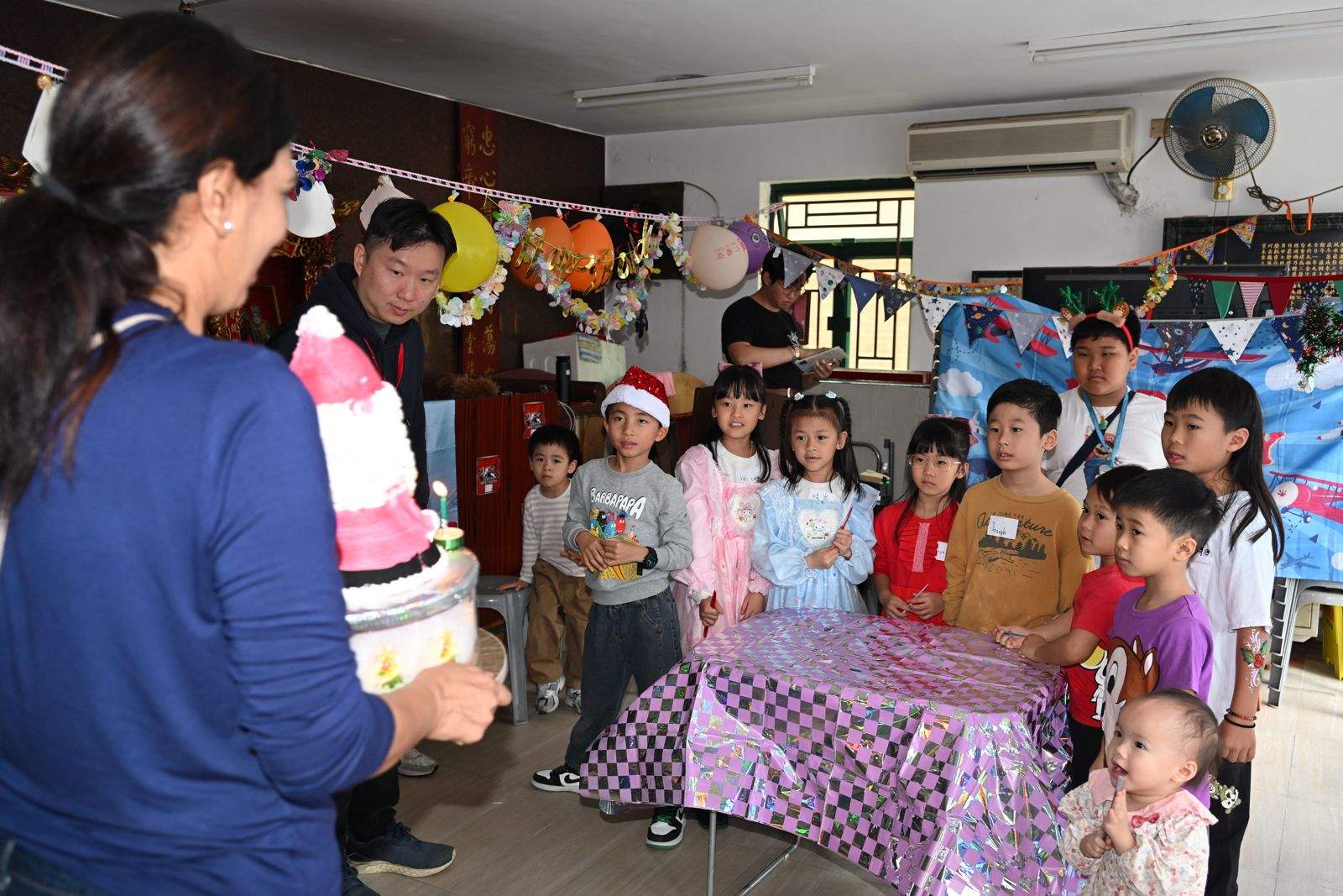 Children line up behind a cake carried towards the table.