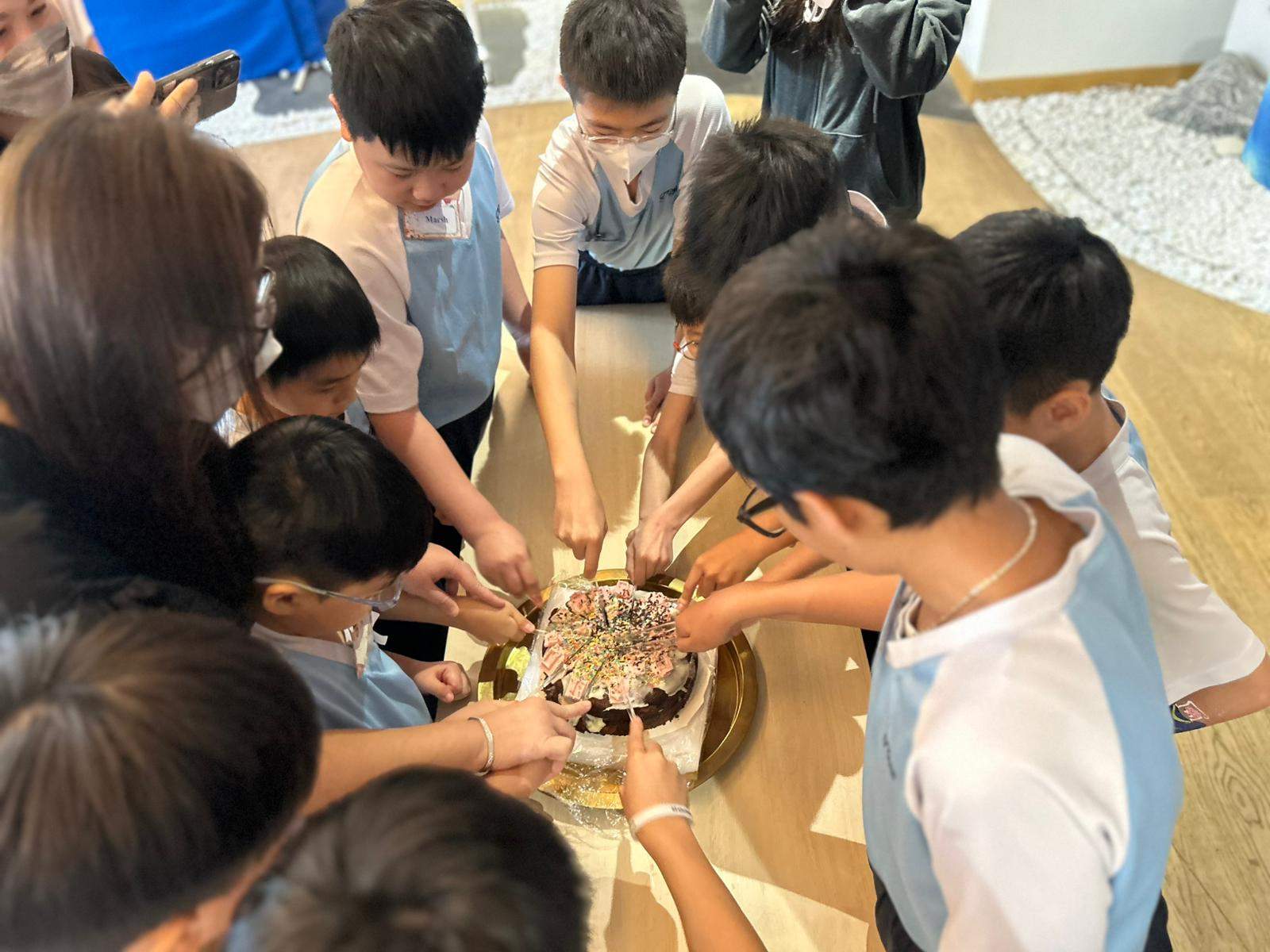 Children crowd around a cake table during cake cutting.