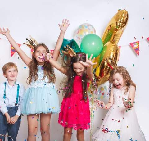 Four children celebrate beneath balloons and falling confetti.