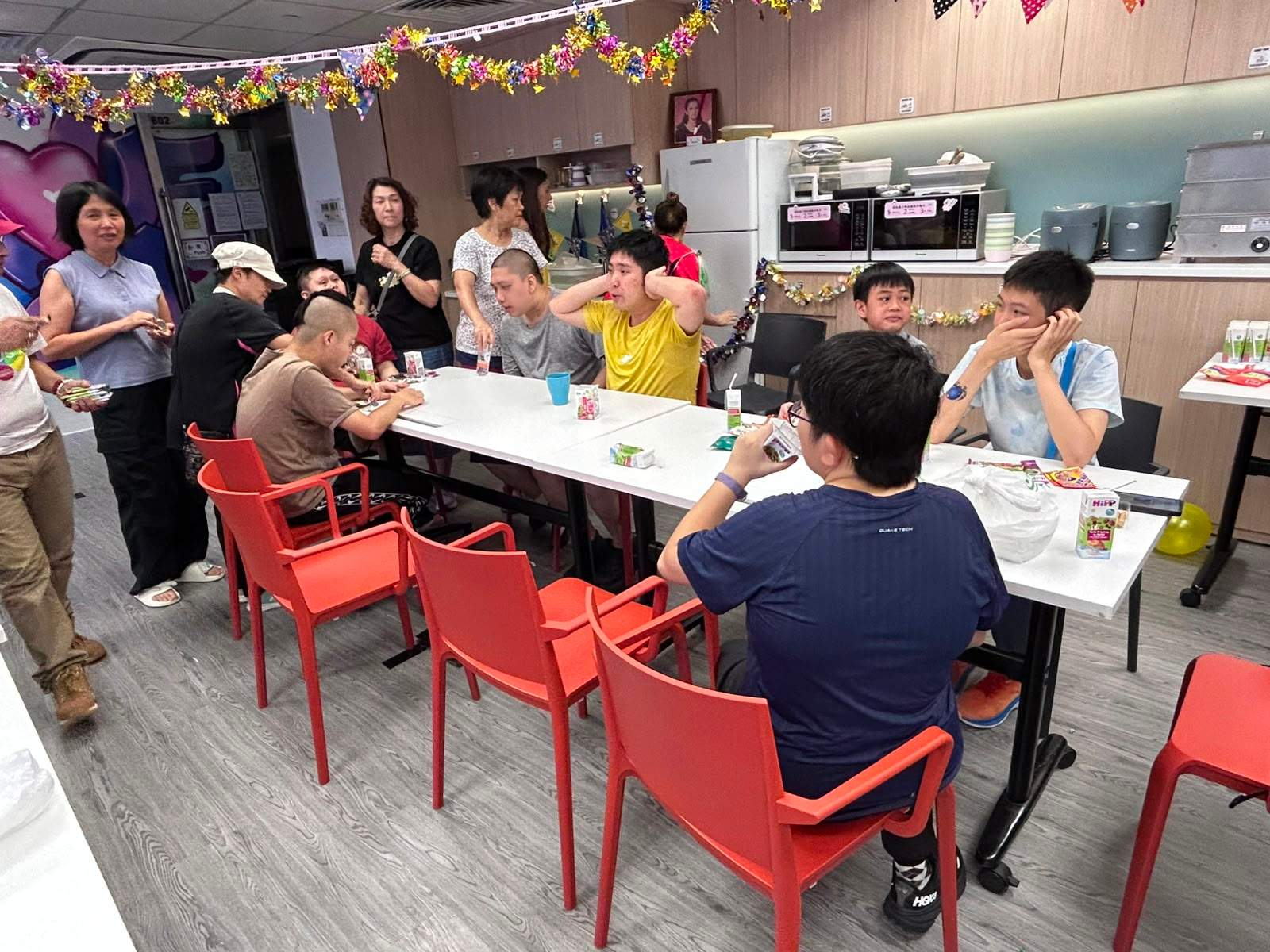 People gather around a long table with cups and snacks.